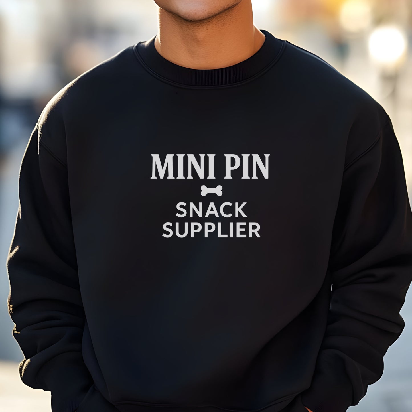 Man wearing a black "Mini Pin Snack Supplier" Miniature Pinscher unisex sweatshirt outdoors in the streets.