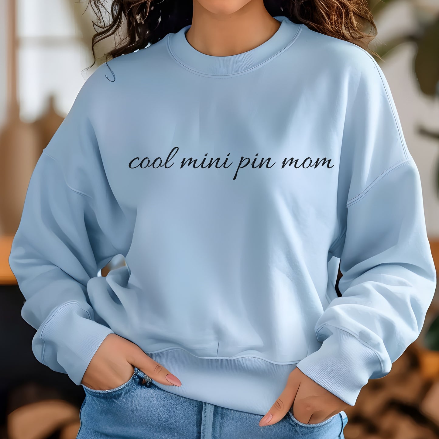 Woman wearing a light blue "cool mini pin mom" Miniature Pinscher women’s sweatshirt, hands in pockets, casual style