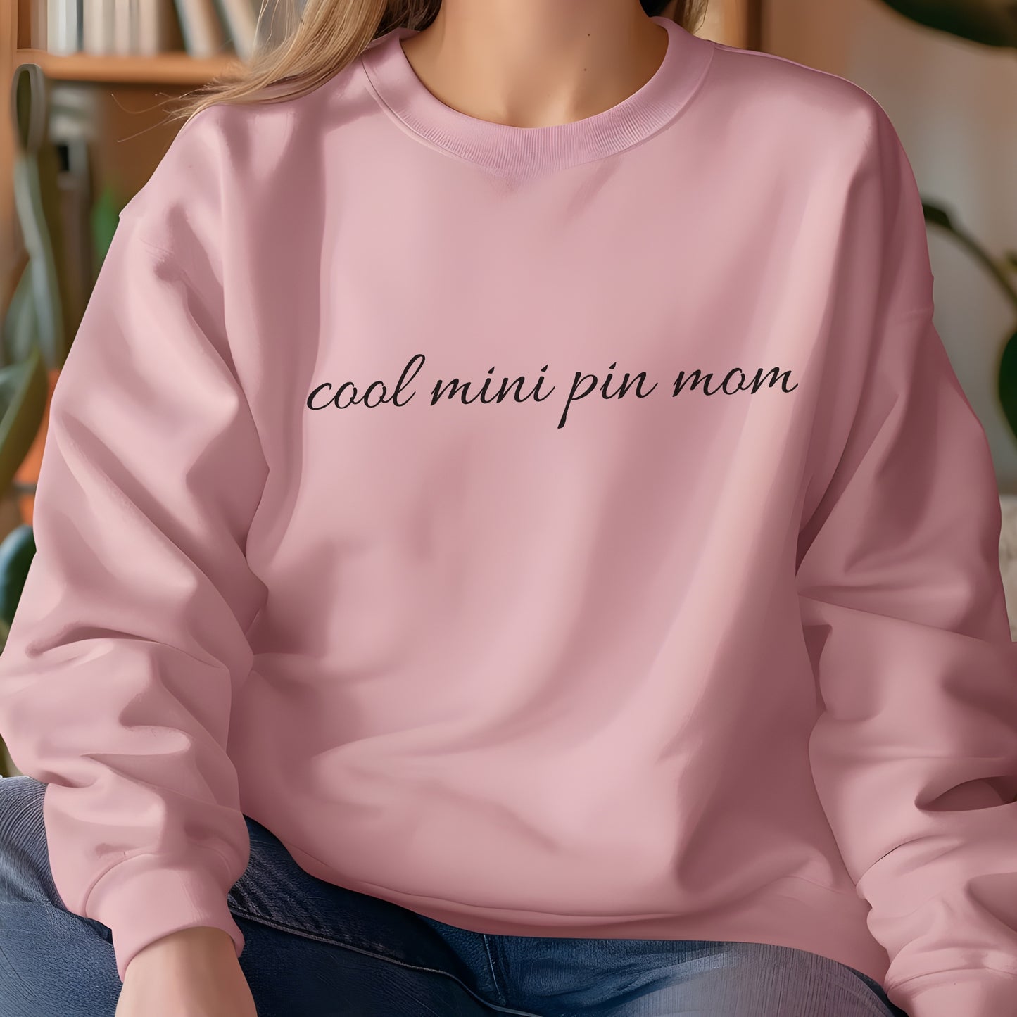 Woman wearing a light pink "cool mini pin mom" Miniature Pinscher women’s sweatshirt, hands in pockets, casual style
