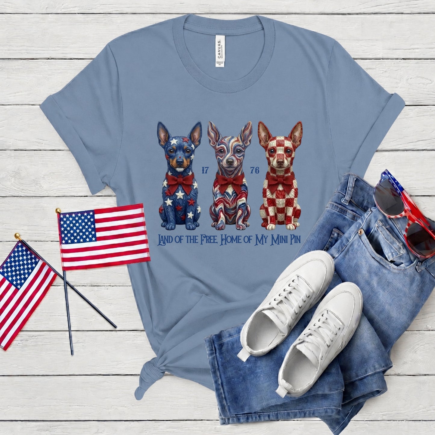 Blue t-shirt with dog illustration, American flags, sneakers, and jeans on a wooden surface