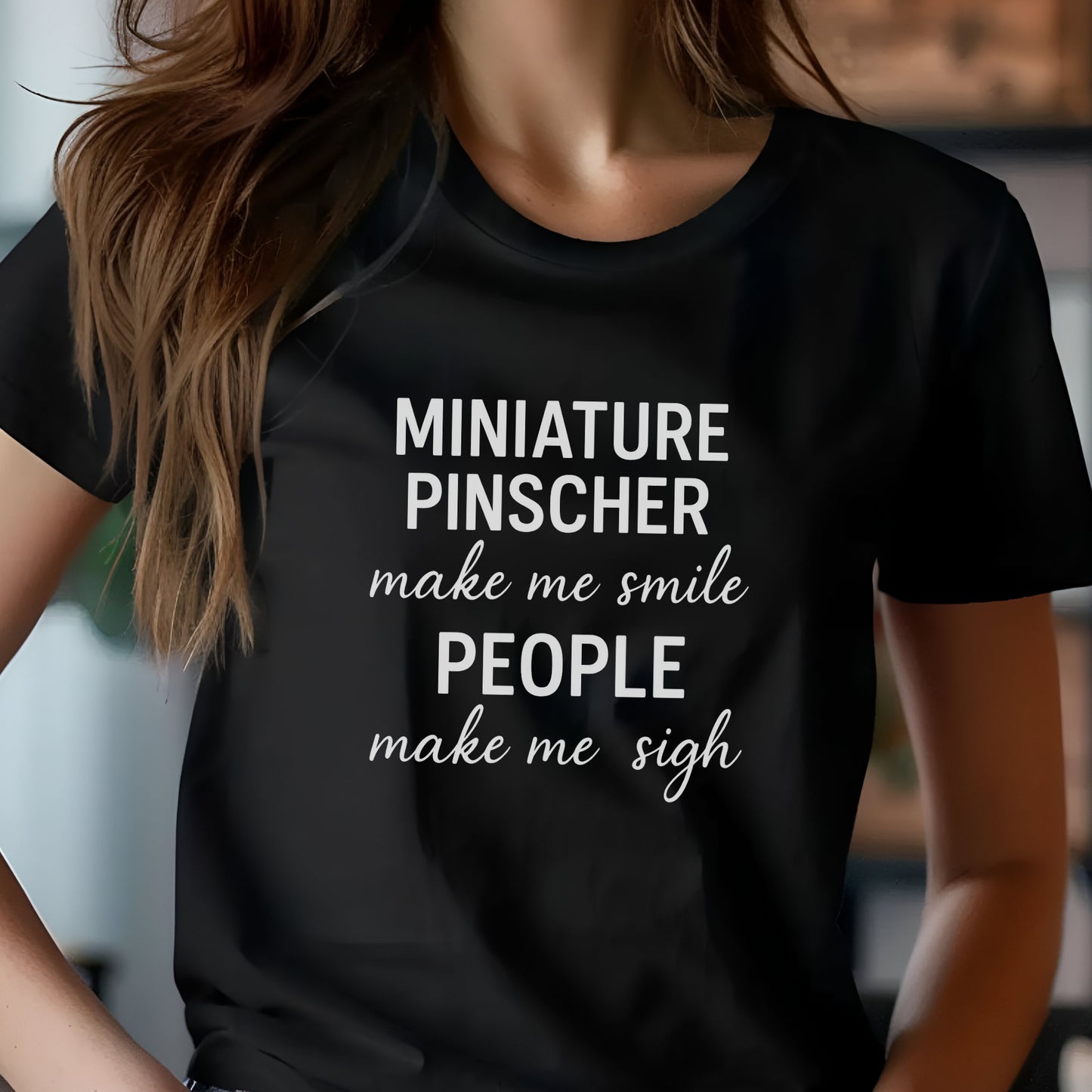 Woman wearing a black "Miniature Pinscher make me smile, people make me sigh" unisex t-shirt, casual kitchen background