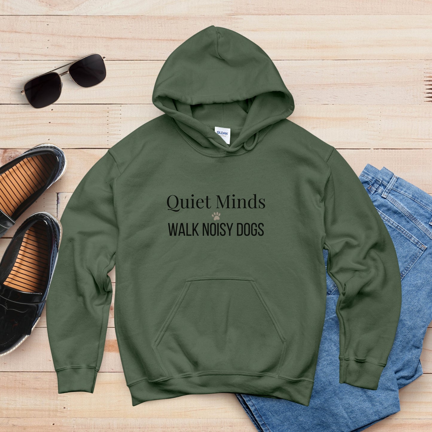 Green hoodie with 'Quiet Minds Walk Noisy Dogs' text on a wooden surface with shoes and sunglasses.