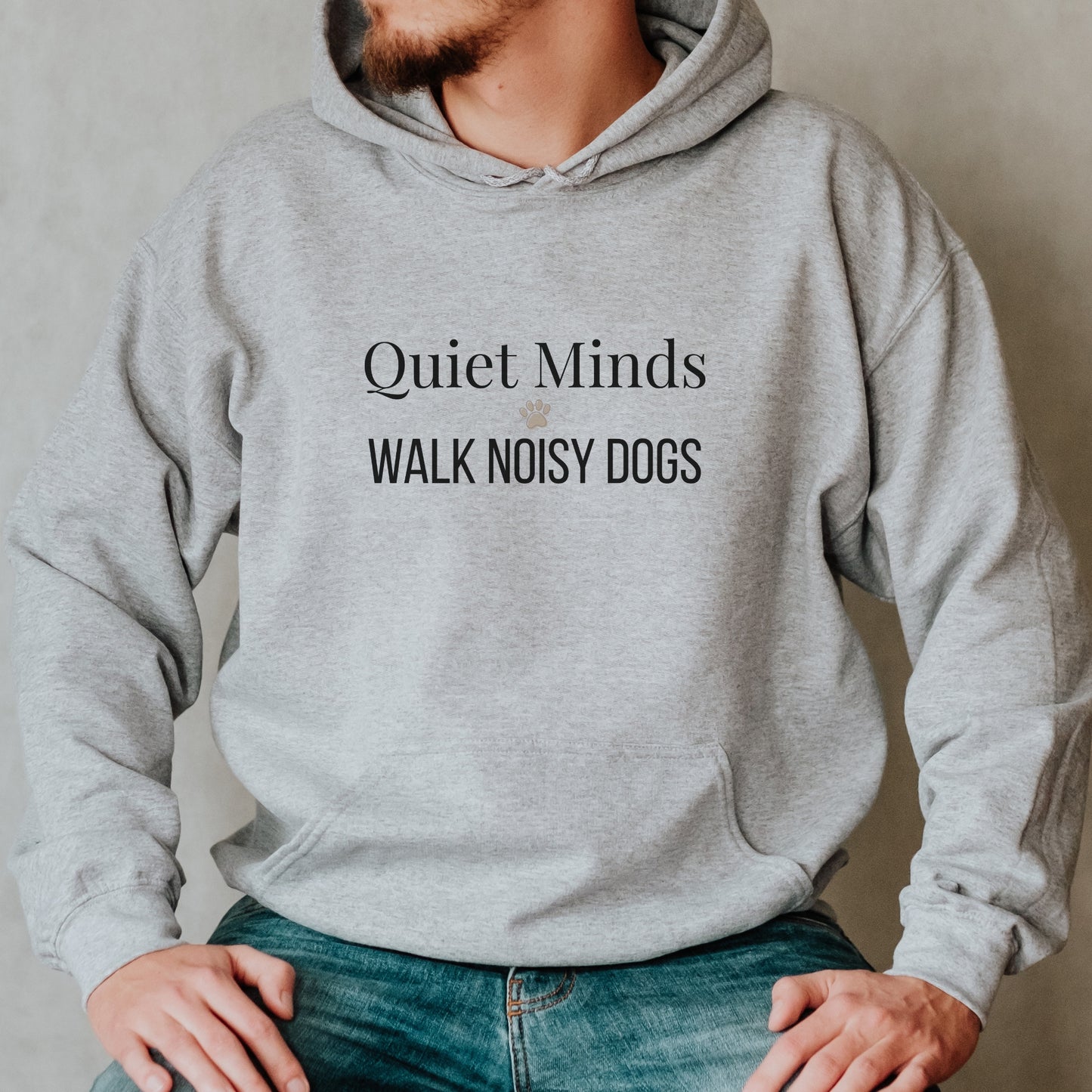 Person wearing a gray hoodie with text 'Quiet Minds Walk Noisy Dogs' on a neutral background