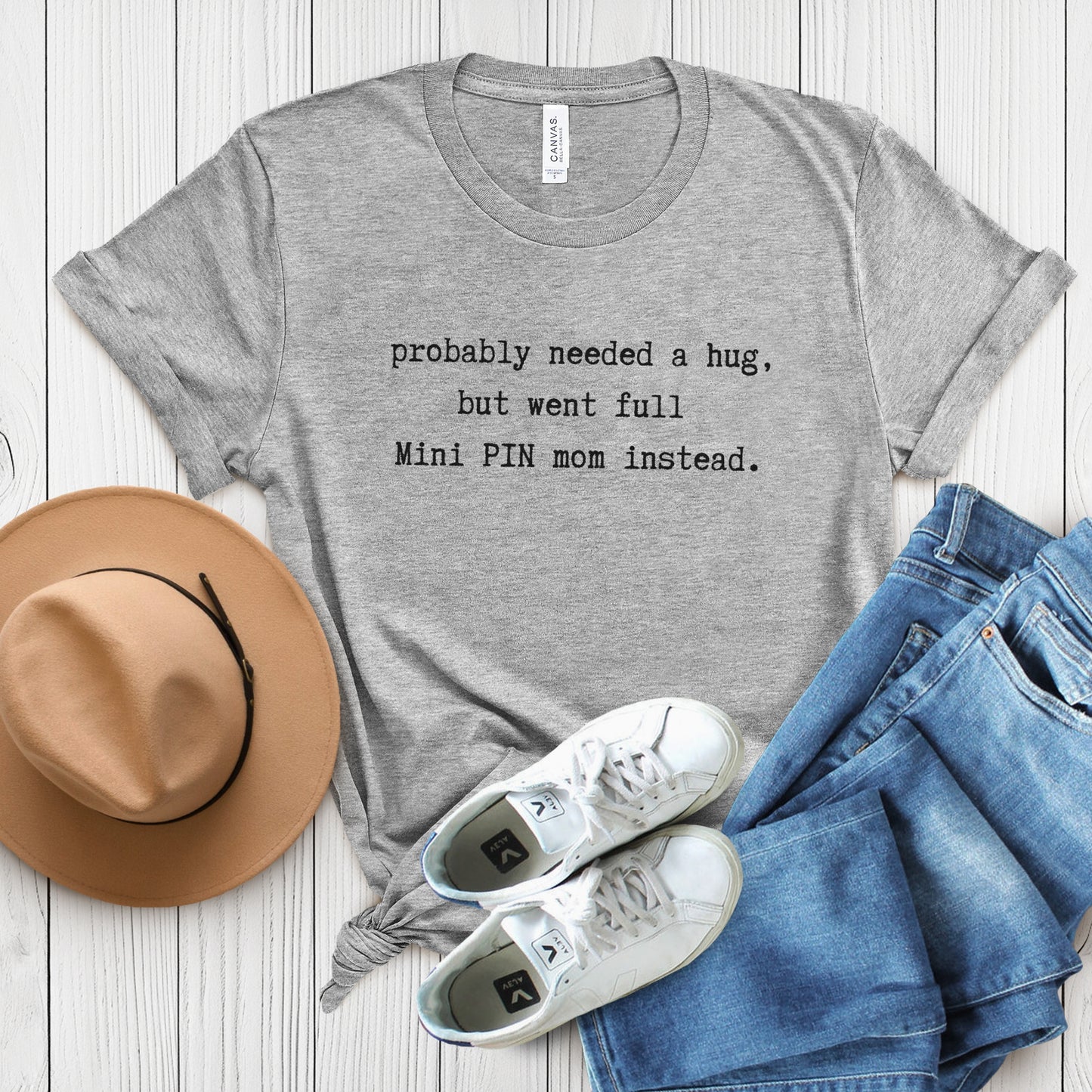 Grey unisex t-shirt flat lay with white text: "probably needed a hug, but went full Mini PIN mom instead." centered on the chest
