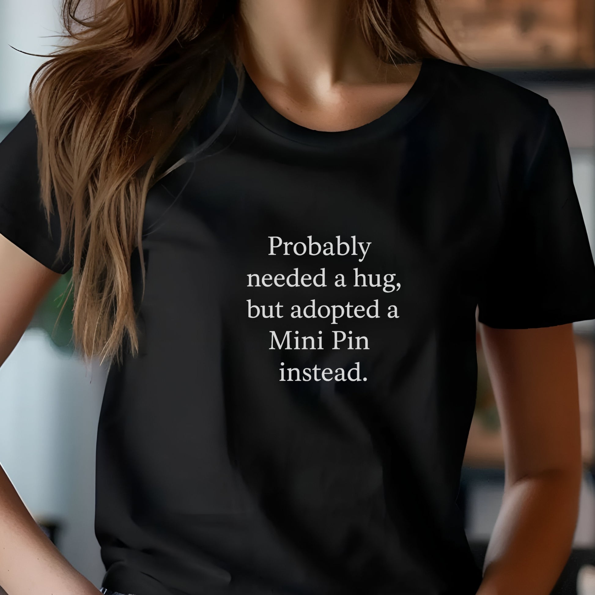 Black unisex t-shirt with white text: "Probably needed a hug, but adopted a Mini Pin instead." displayed on plain background 