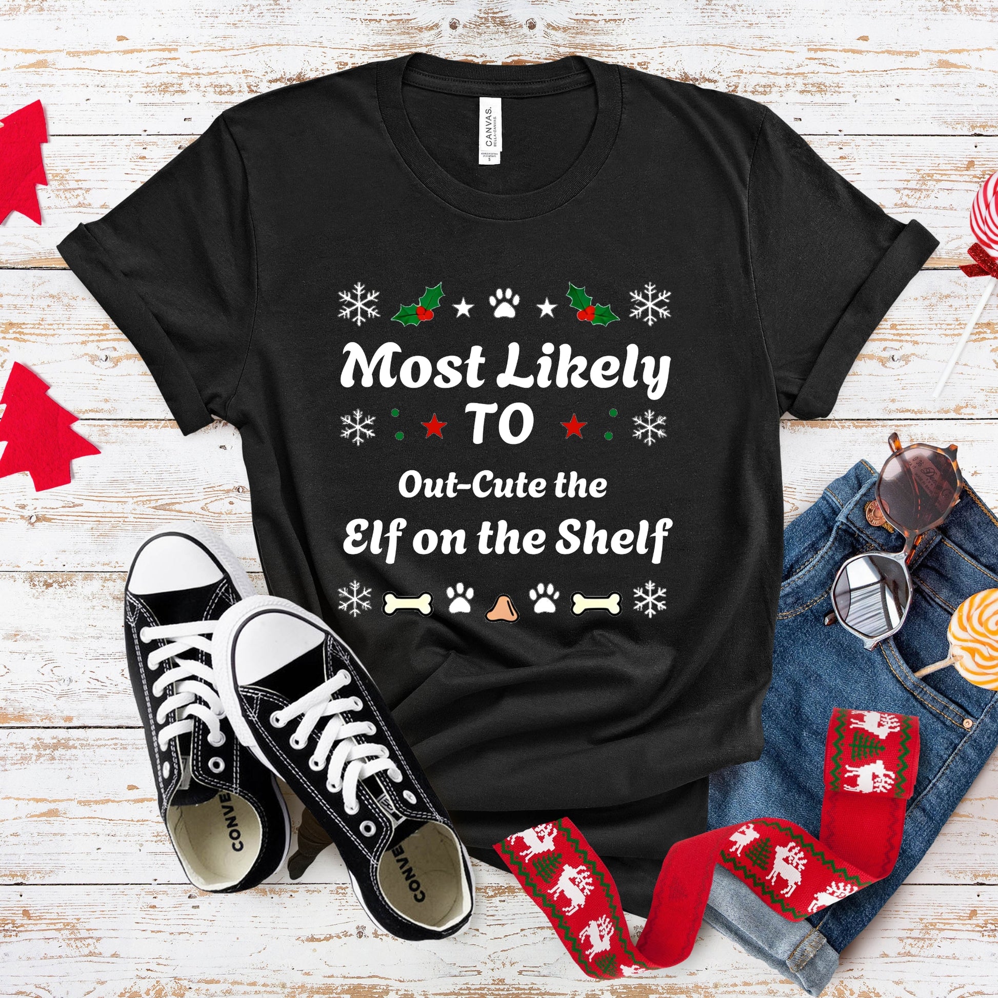 Black t-shirt with Christmas-themed text, sneakers, and festive socks on a wooden surface