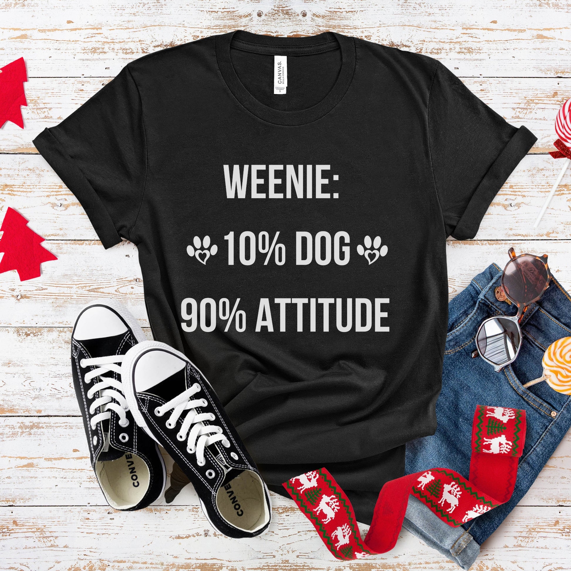 Black t-shirt with 'Weenie: 10% Dog 90% Attitude' text, paired with sneakers and socks on a wooden surface.