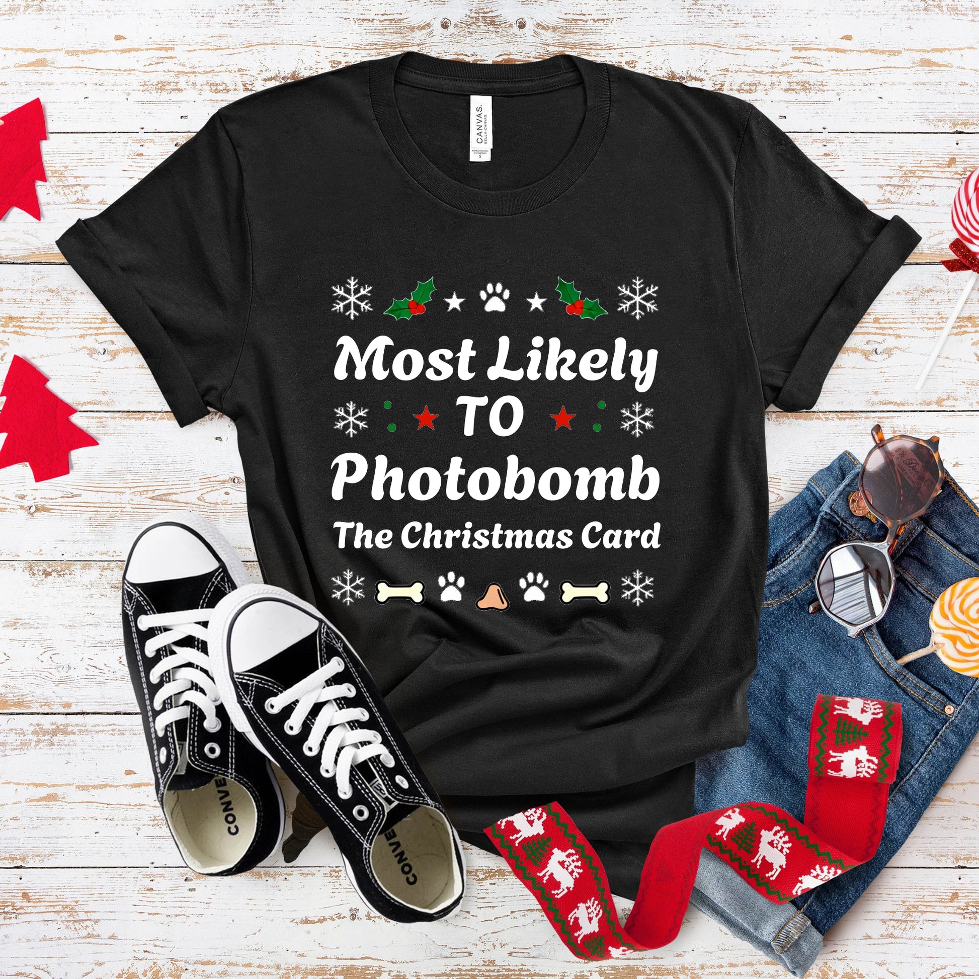 Black t-shirt with Christmas-themed text, sneakers, socks, and jeans on a wooden surface