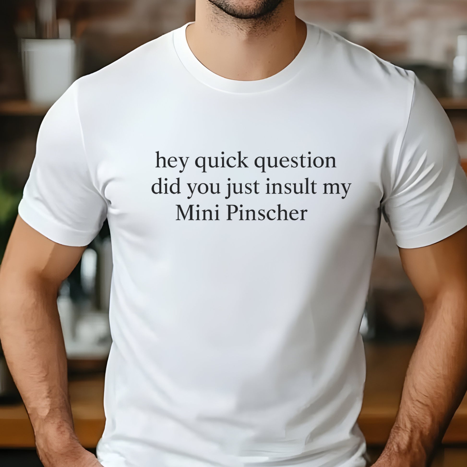 Man wearing a white "hey quick question did you just insult my Mini Pinscher" t-shirt, standing by a window