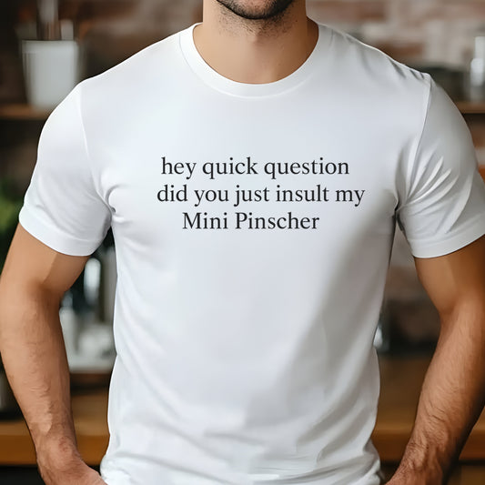 Man wearing a white "hey quick question did you just insult my Mini Pinscher" t-shirt, standing by a window