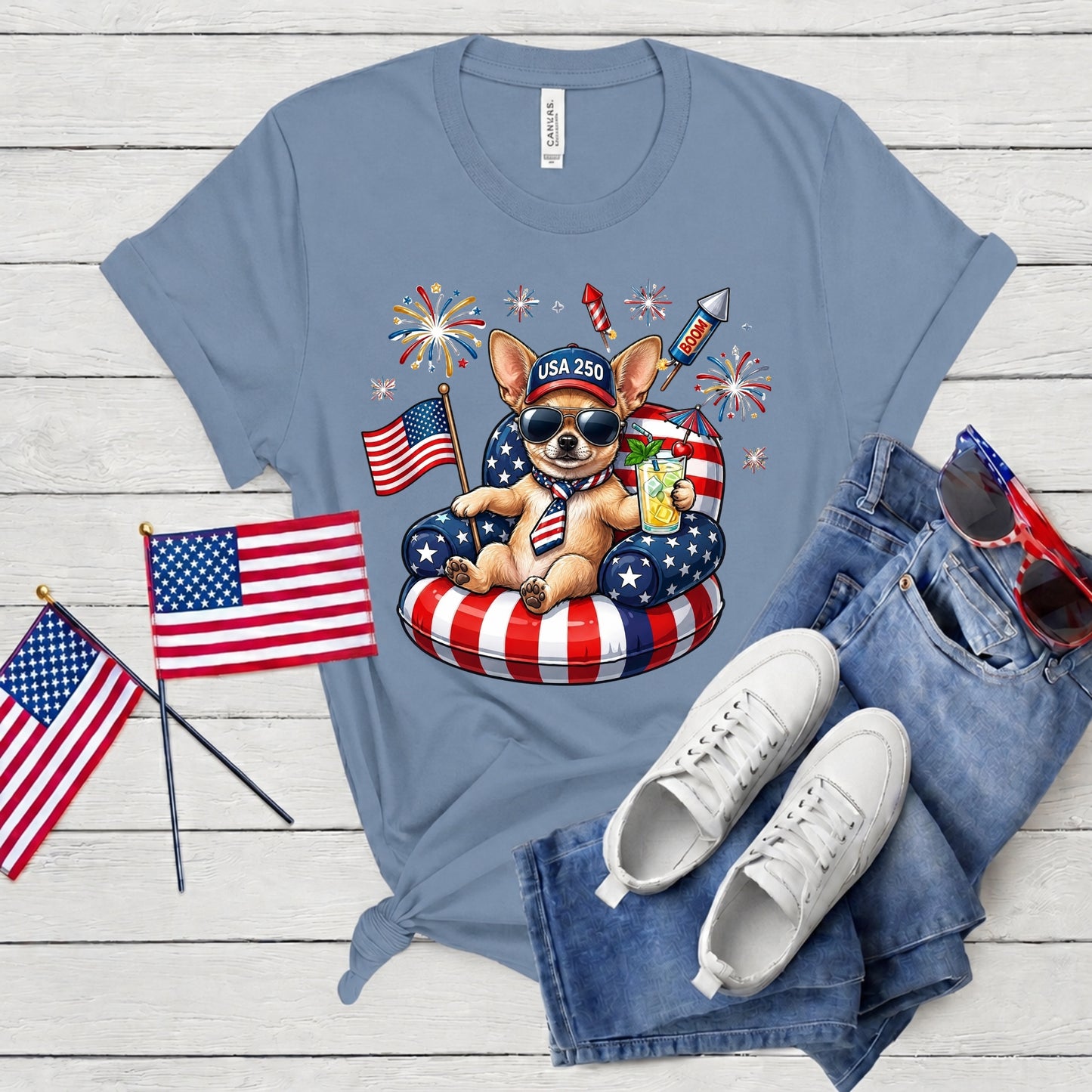 Blue t-shirt with a dog graphic, American flags, and sunglasses on a wooden surface.