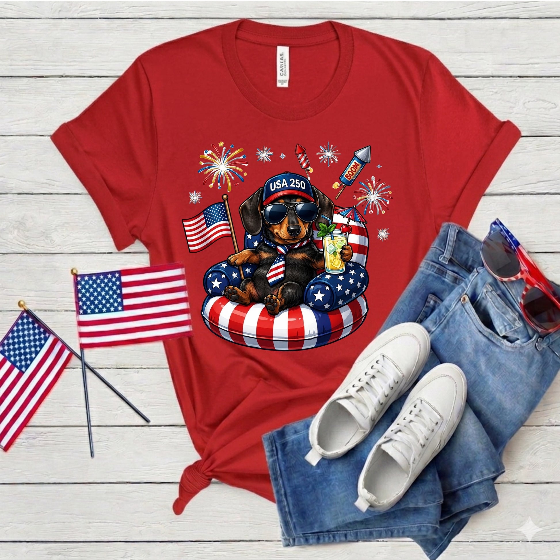 Red t-shirt with a dachshund graphic, American flags, and sunglasses on a wooden surface.
