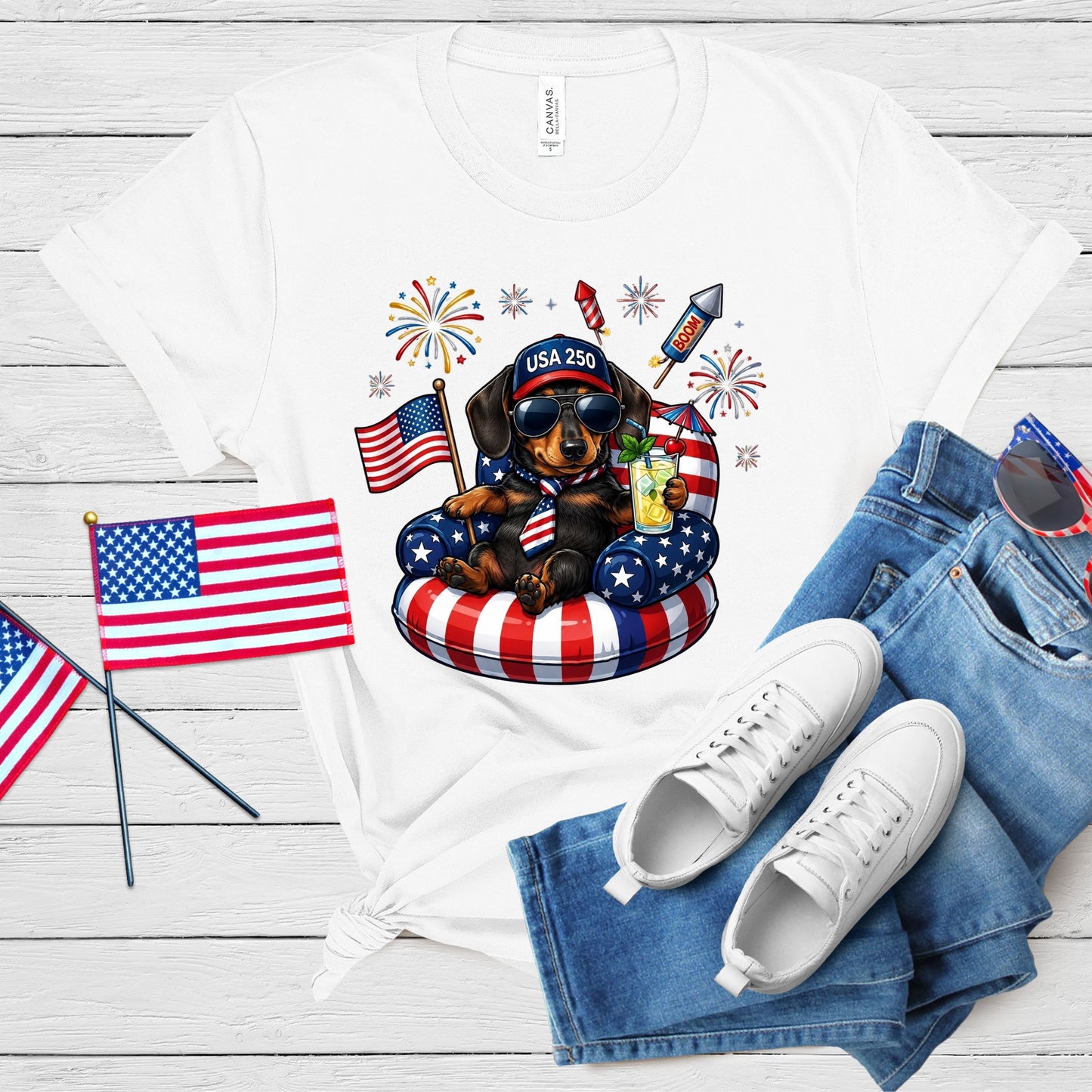 White t-shirt with a dog graphic, American flags, and white sneakers on a wooden surface.