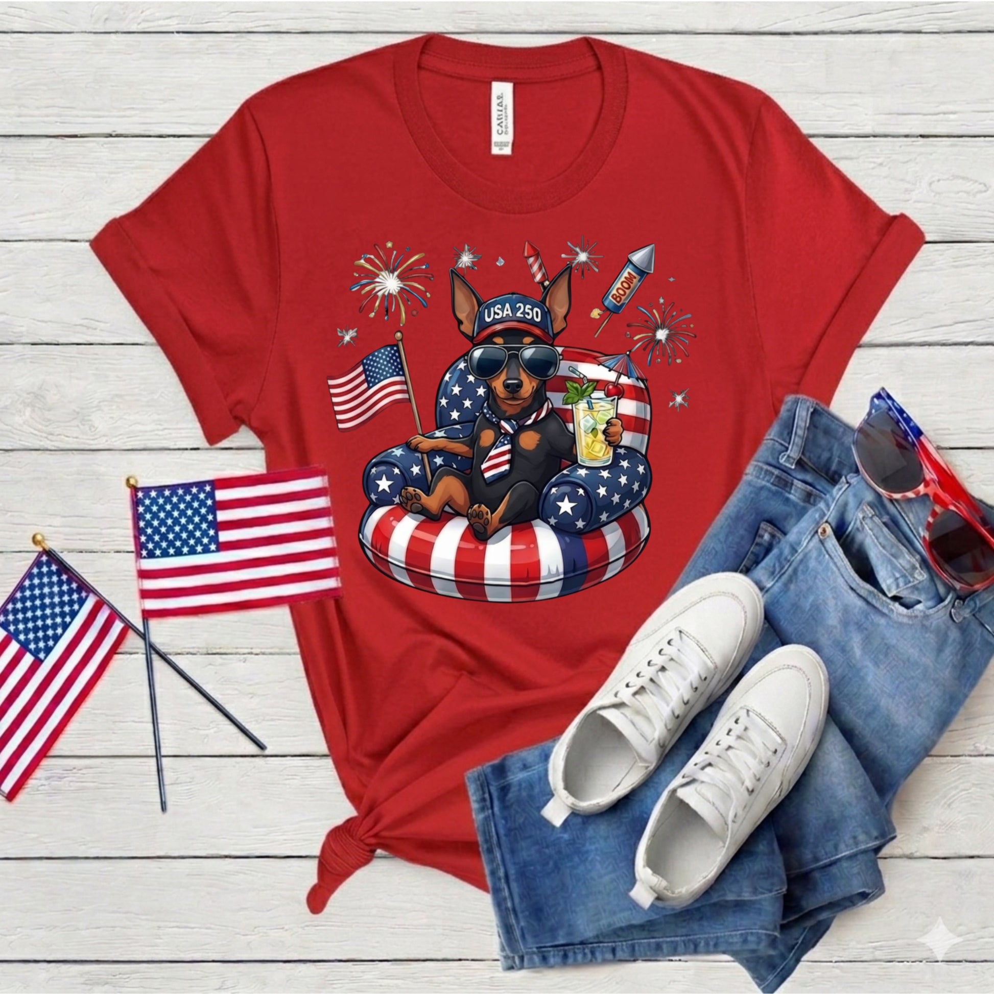 Red t-shirt with a dog graphic, American flags, and sunglasses on a wooden surface.