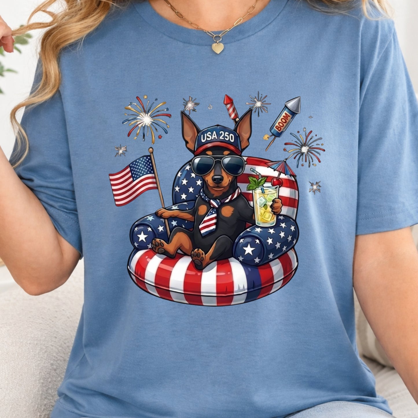 Person wearing a blue t-shirt with a graphic of a dog on an inner tube, American flag, and fireworks.