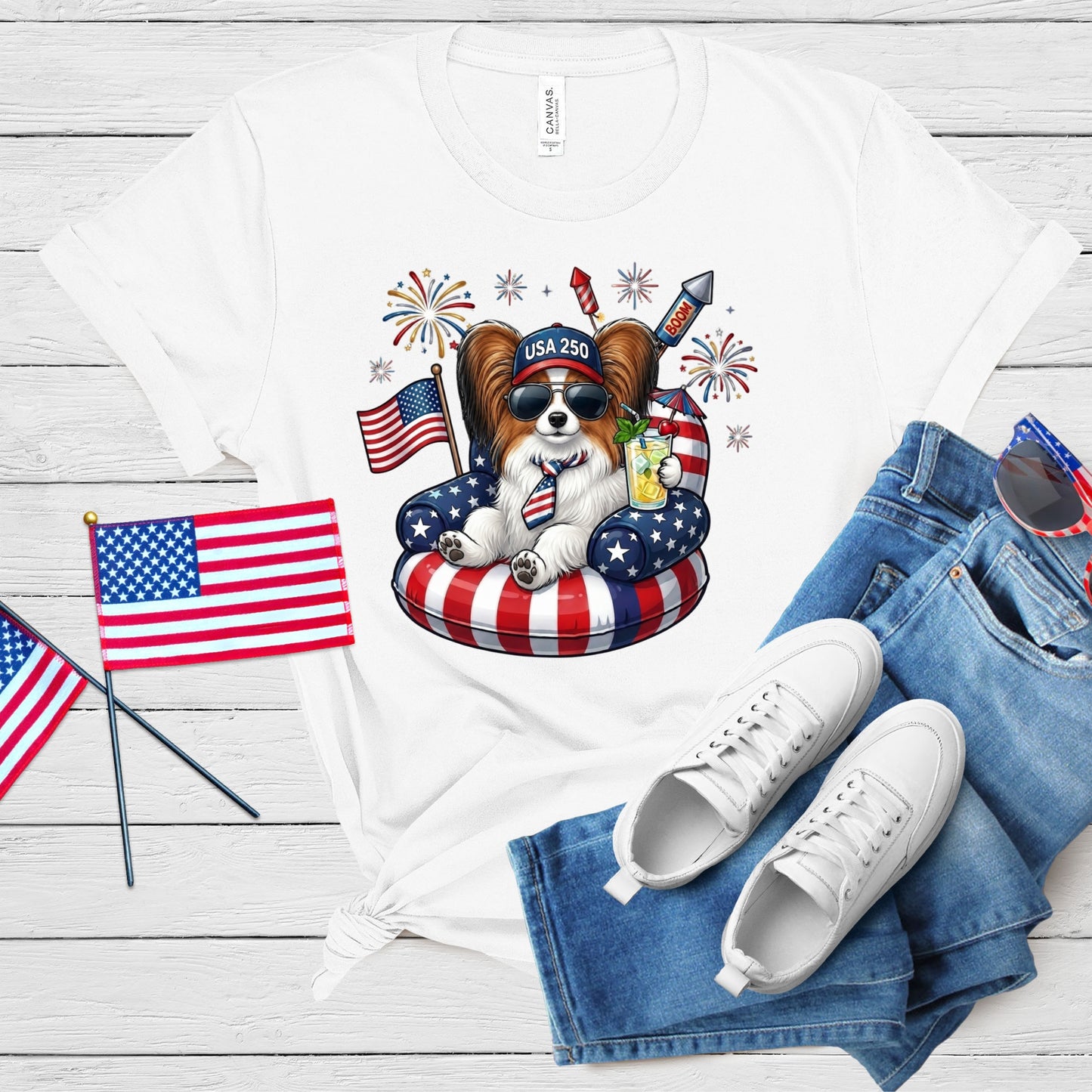White t-shirt with a dog graphic, American flags, and jeans on a wooden surface