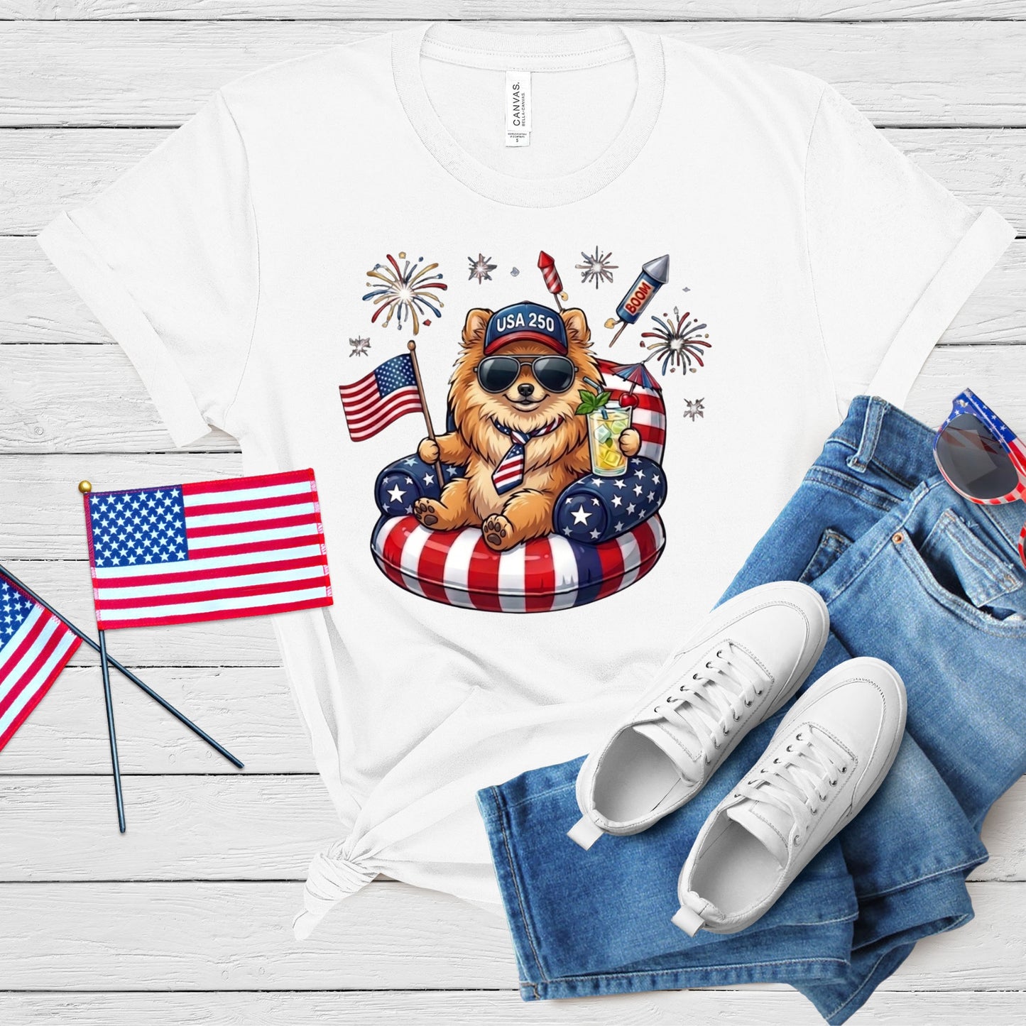 White t-shirt with a bear graphic, American flags, and sunglasses on a wooden surface.