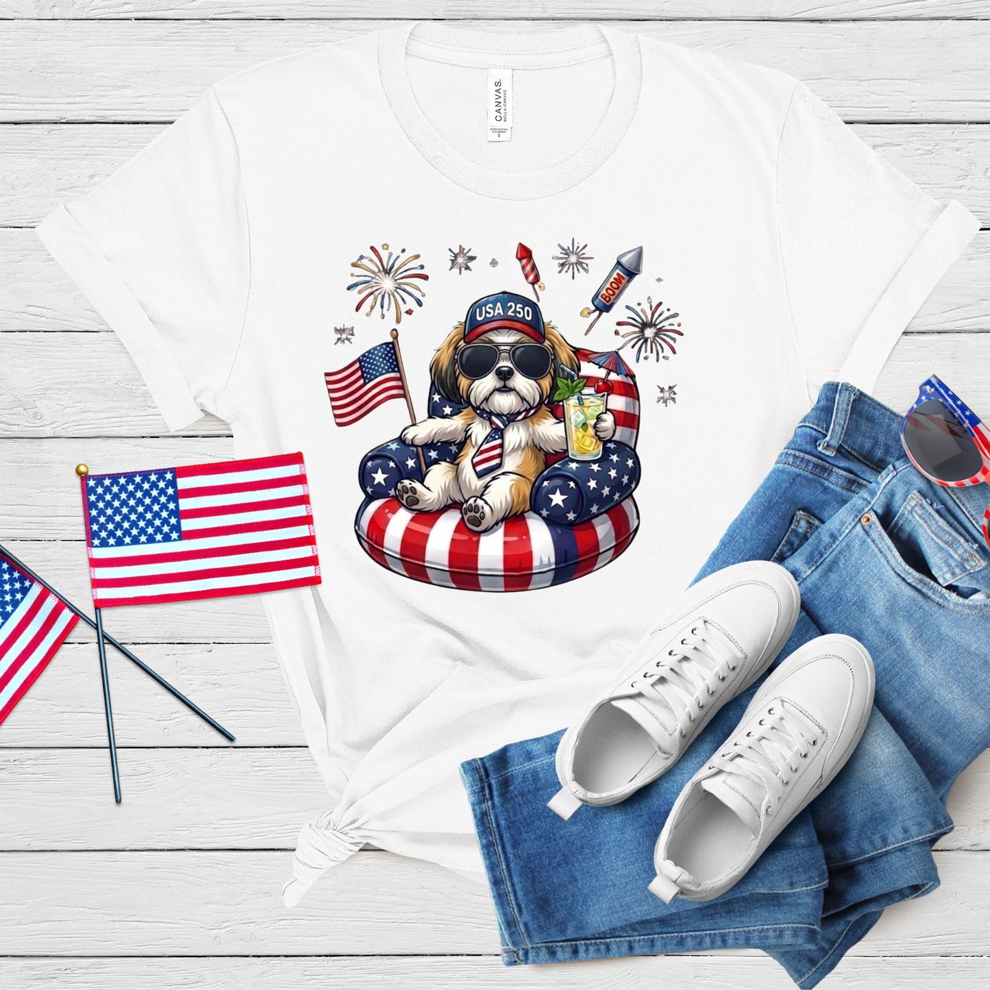 White t-shirt with a dog graphic, American flags, and white sneakers on a wooden surface.