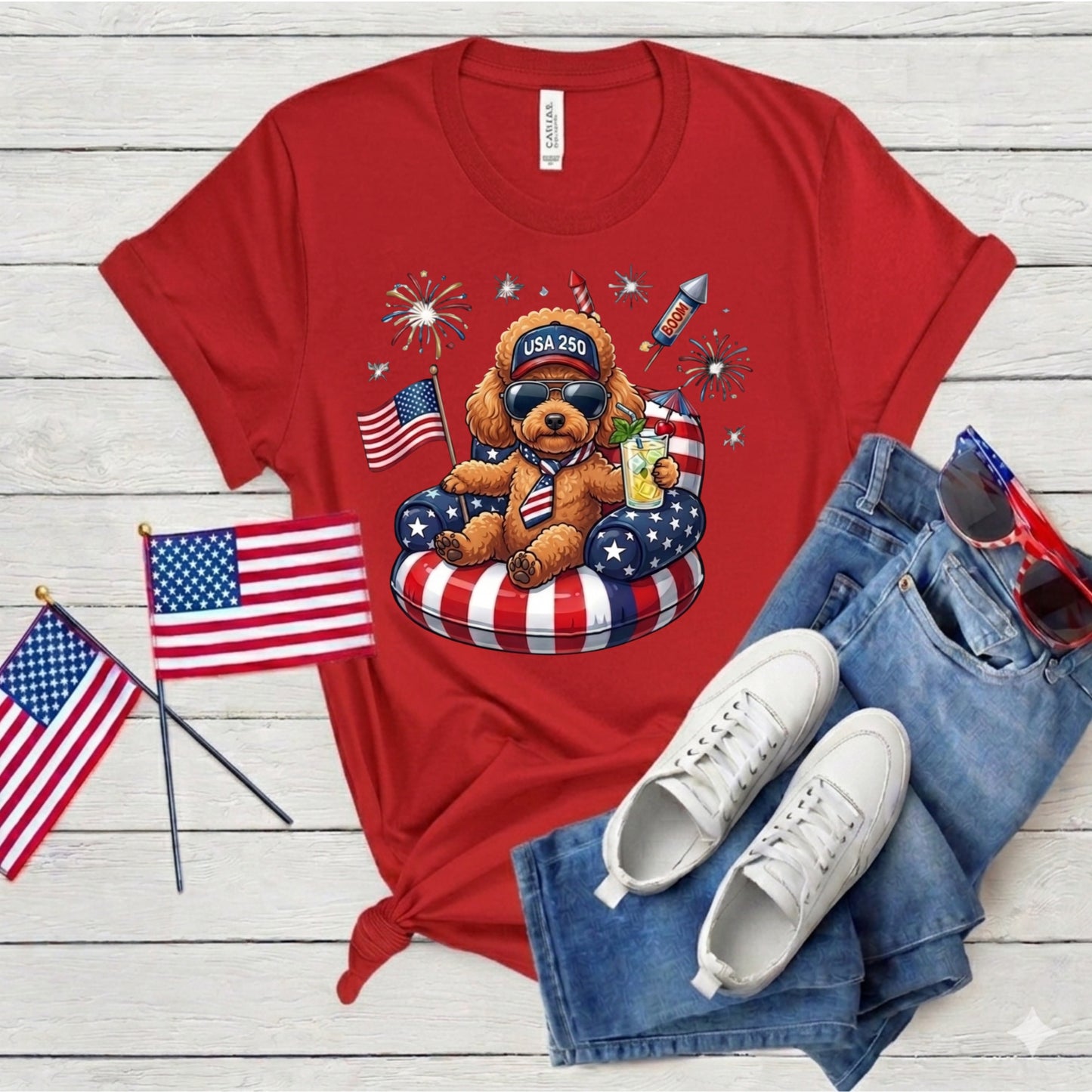 Red t-shirt with a teddy bear graphic, American flags, and sunglasses on a wooden surface.