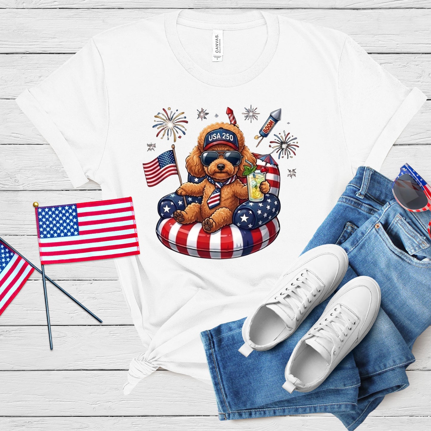 White t-shirt with a bear graphic, American flags, and sunglasses on a wooden surface.