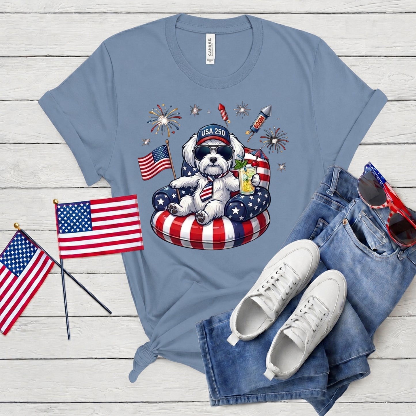 Blue t-shirt with a dog graphic, American flags, and sunglasses on a wooden surface