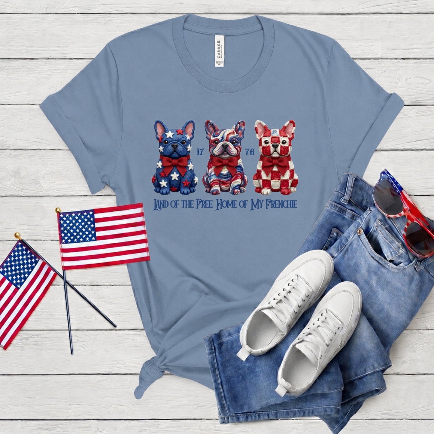 Blue t-shirt with dog graphics and text, paired with American flags, sneakers, and jeans on a wooden surface.