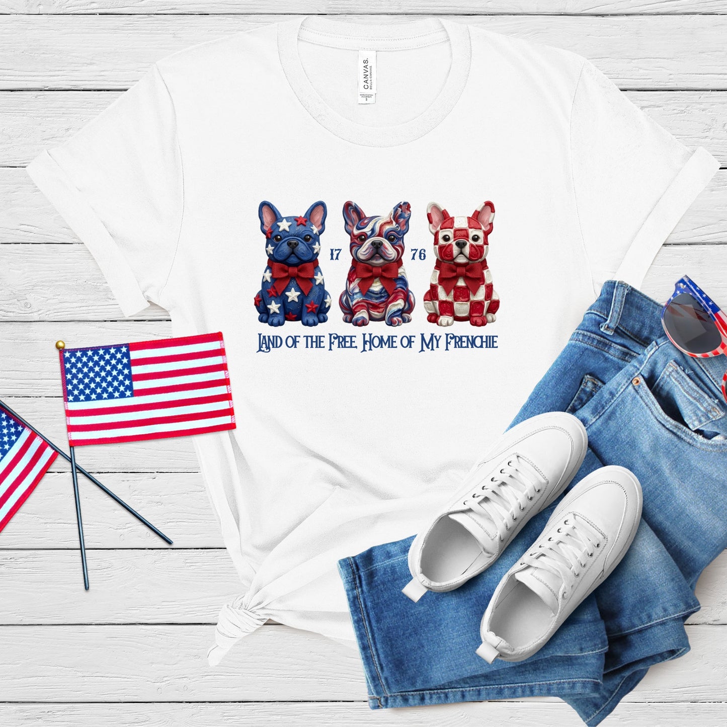 White t-shirt with dog illustration, American flags, and jeans on a wooden surface