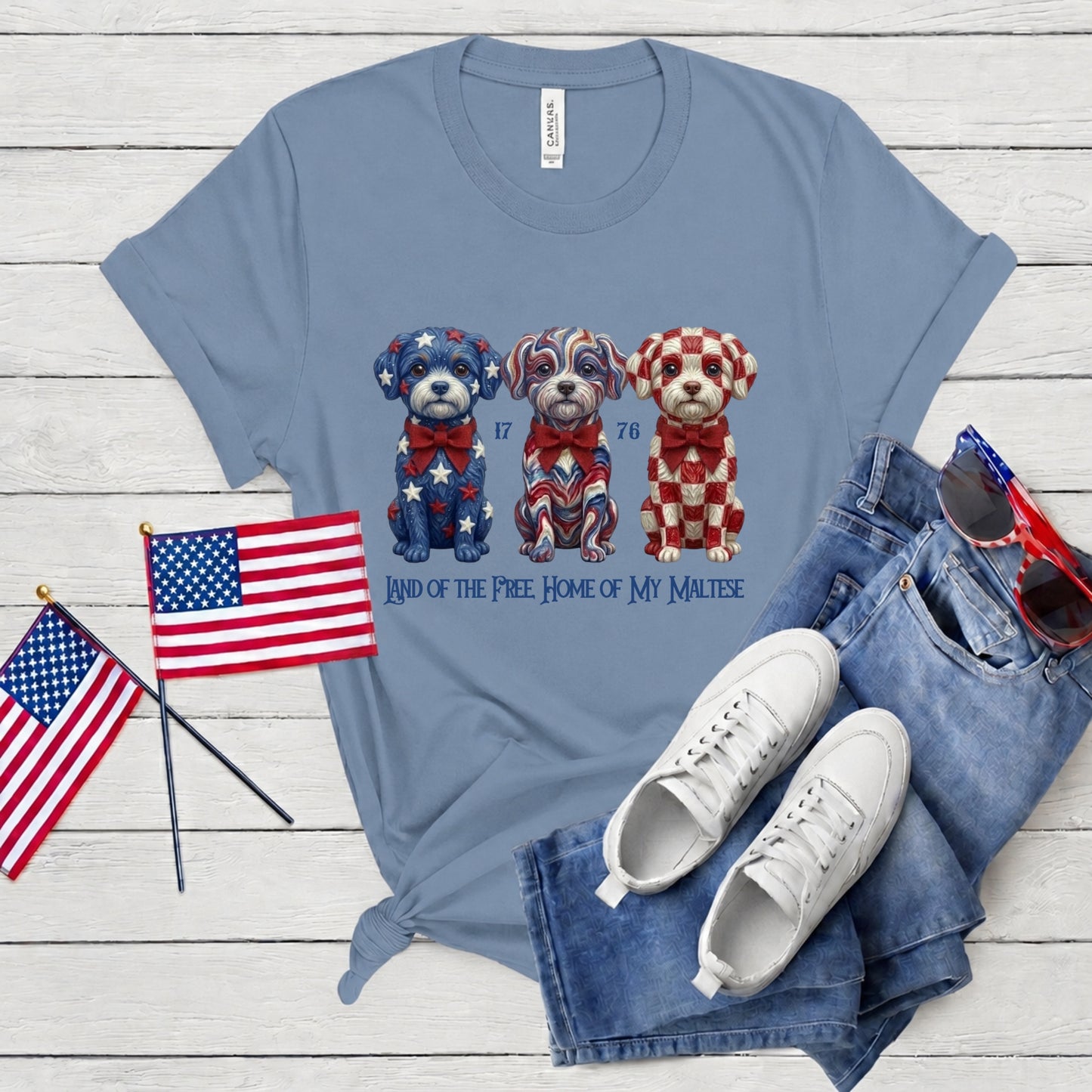 Blue t-shirt with dog graphic, American flags, white sneakers, and denim shorts on a wooden surface.