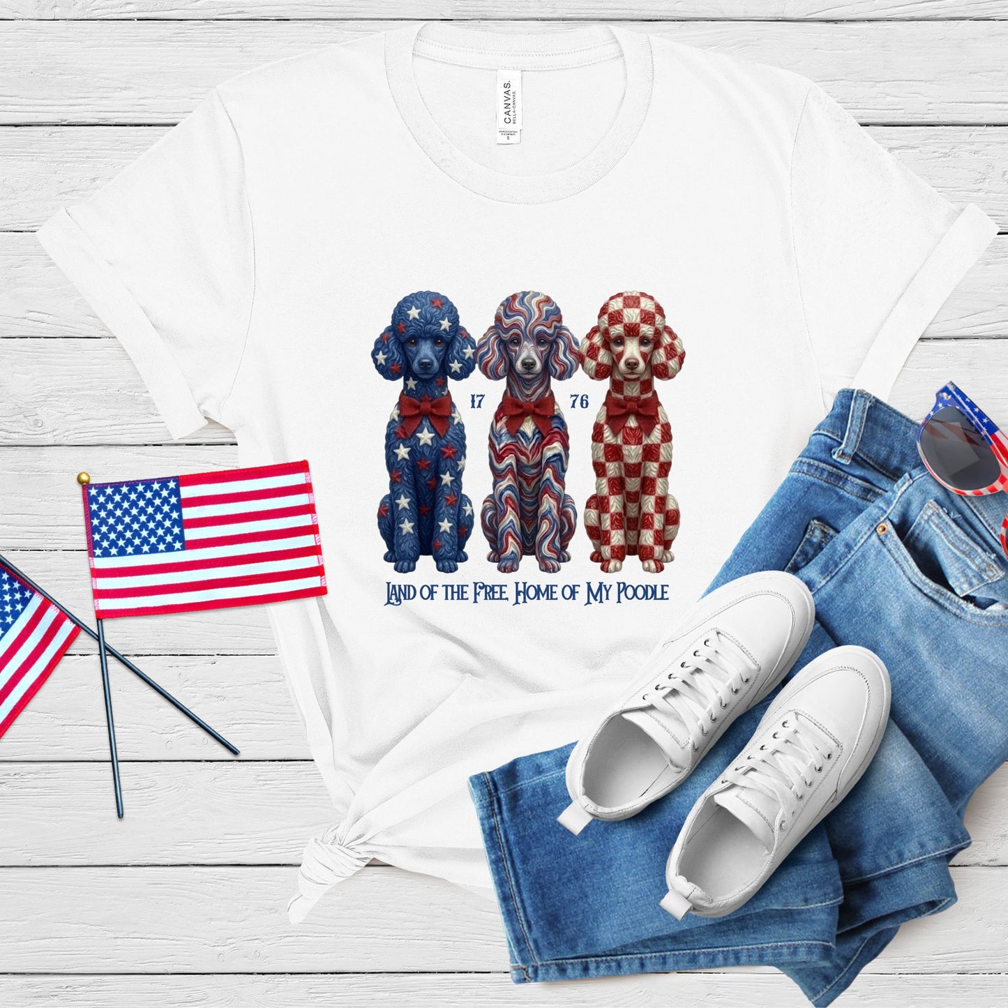 White t-shirt with dog illustration, American flags, jeans, and sneakers on a wooden surface