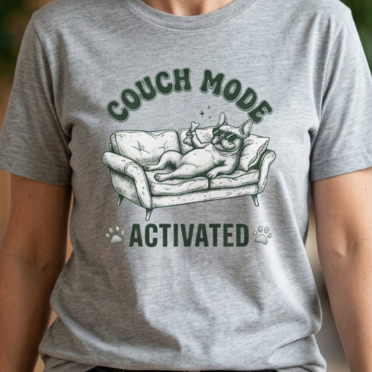 Gray t-shirt with a graphic of a dog on a couch and text 'Couch Mode Activated' on a neutral background.