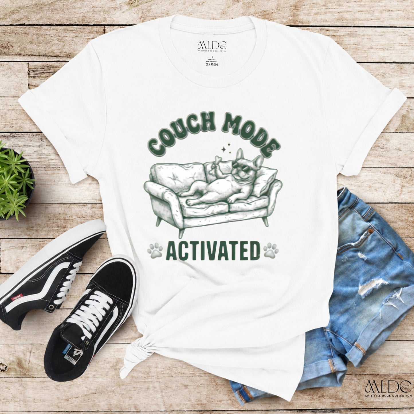White t-shirt with 'Couch Mode Activated' graphic on a wooden surface with shoes and jeans.