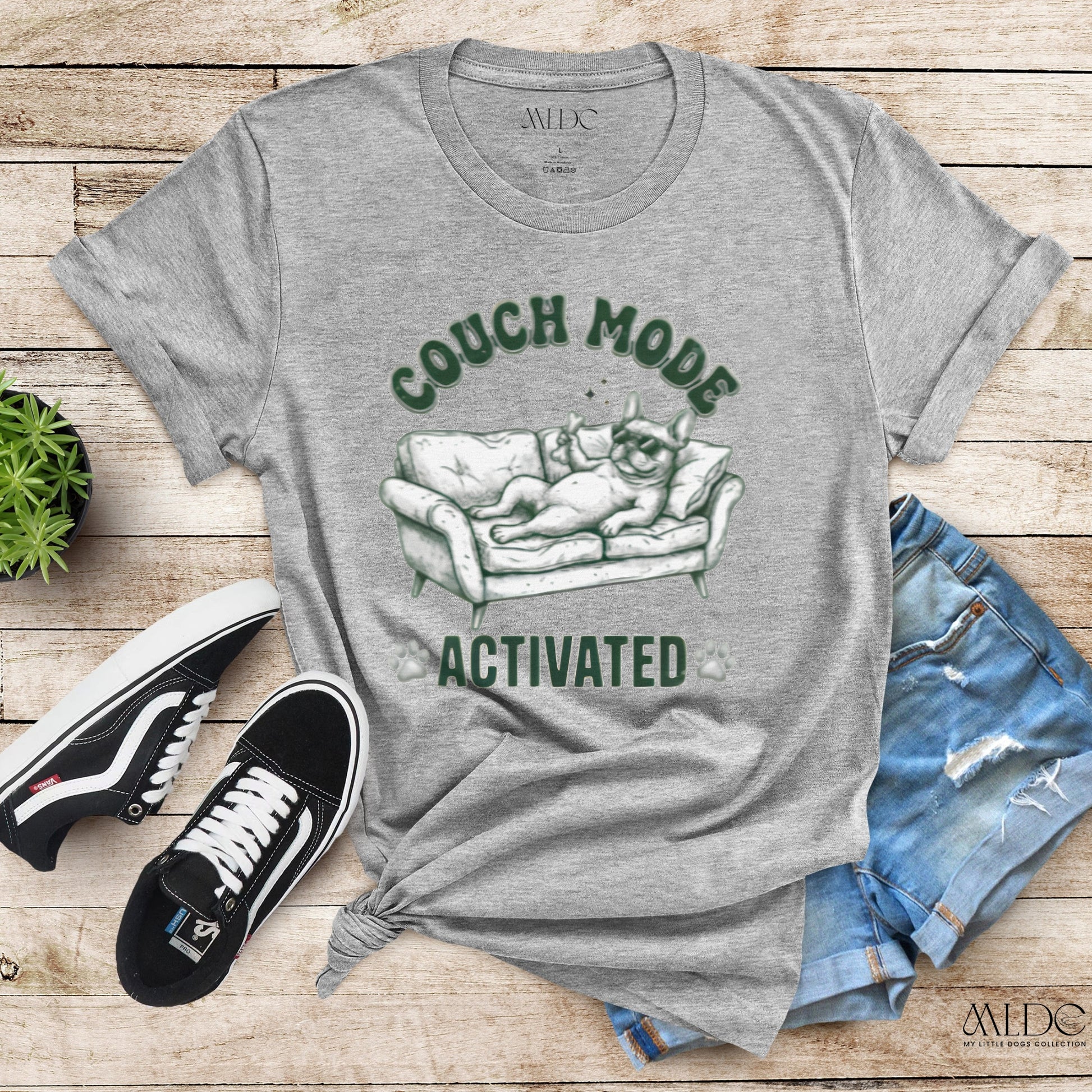 Gray t-shirt with 'Couch Mode Activated' graphic on a wooden surface with sneakers and shorts.