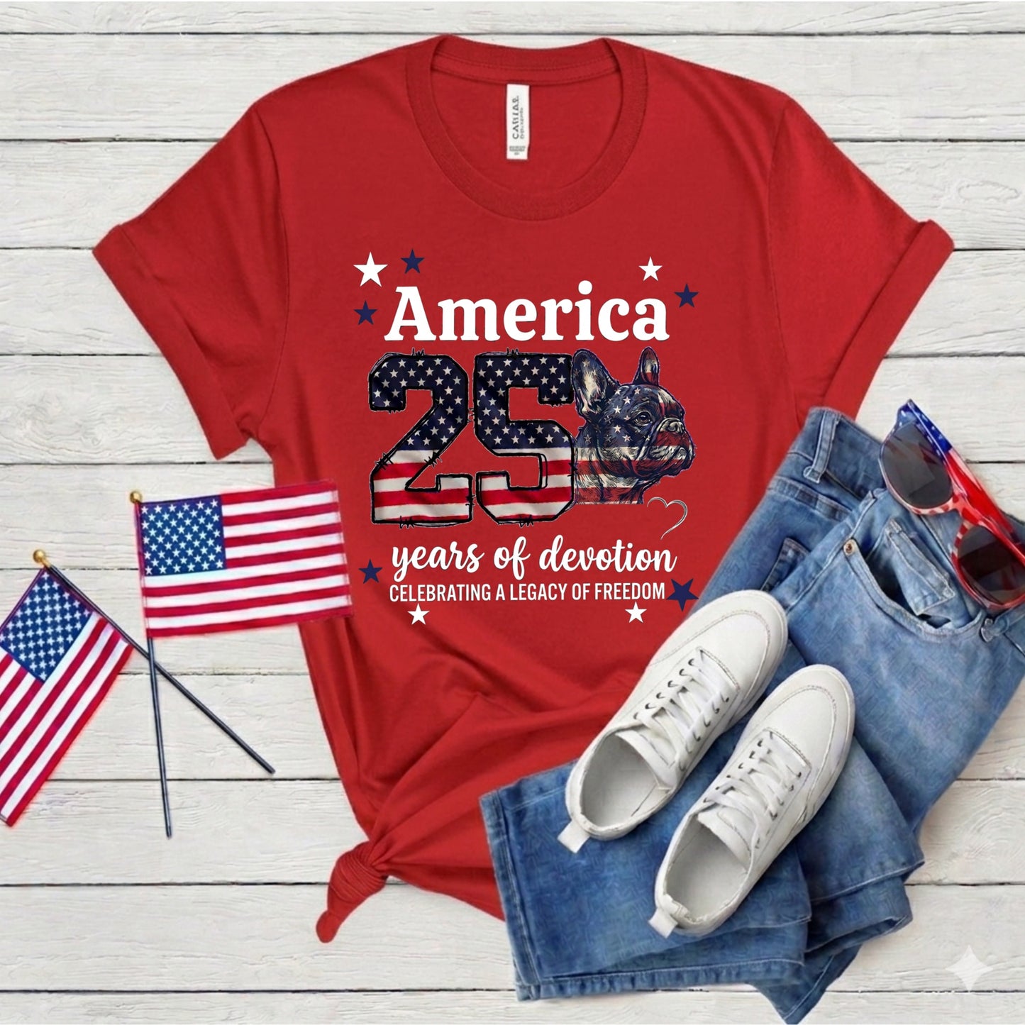 Red t-shirt with American-themed design, white sneakers, blue jeans, and American flags on a wooden surface.
