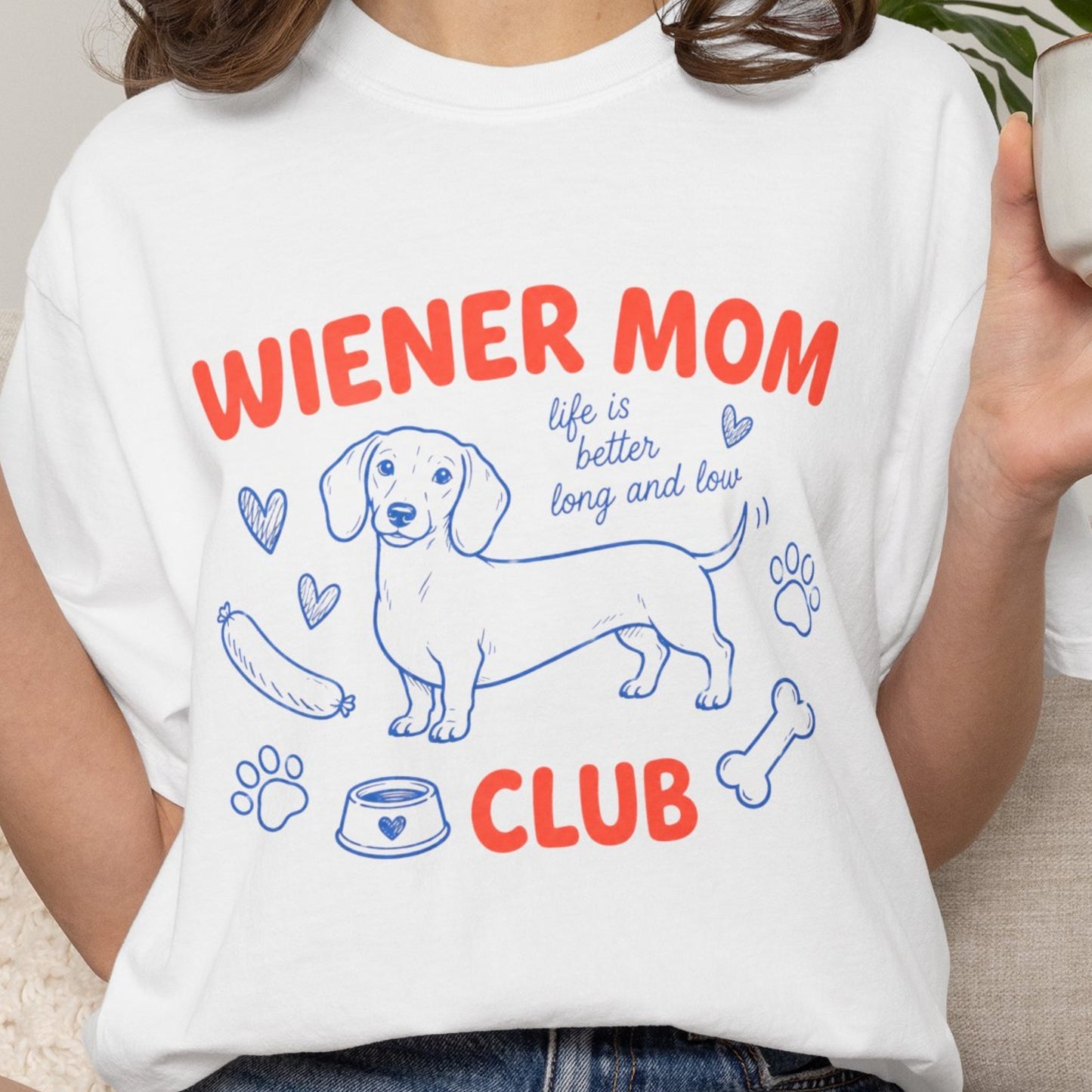 Person wearing a white t-shirt with 'Wiener Mom Club' design featuring a dachshund illustration.