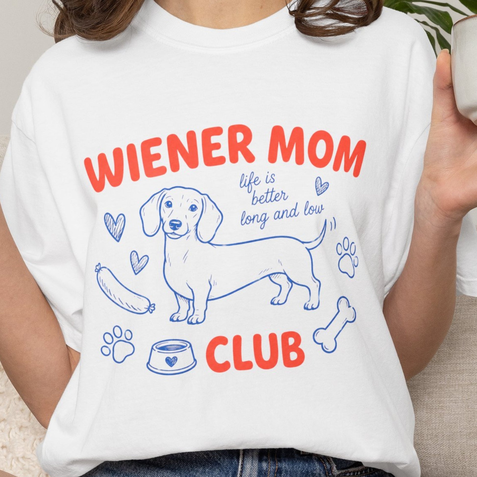 Person wearing a white t-shirt with 'Wiener Mom Club' design featuring a dachshund illustration.