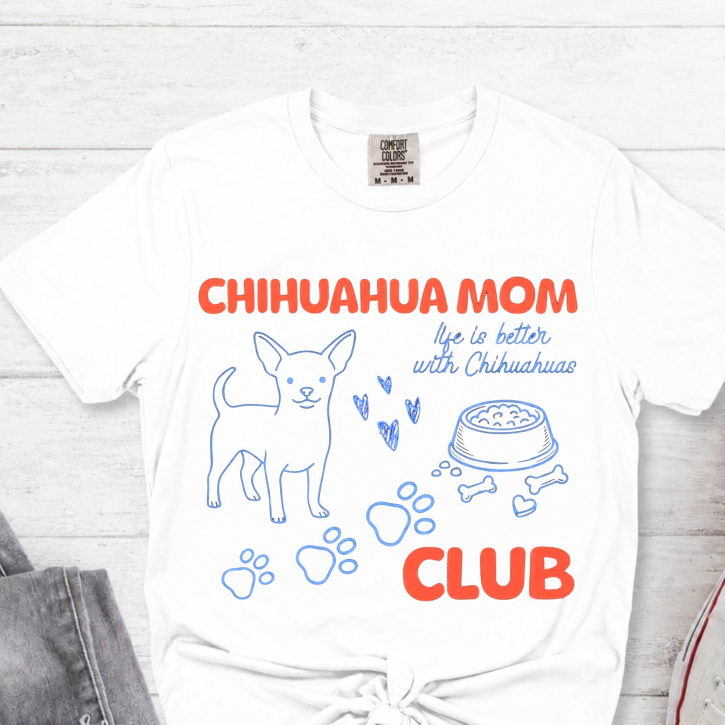 White t-shirt with 'Chihuahua Mom Club' text and graphics on a light wooden surface.