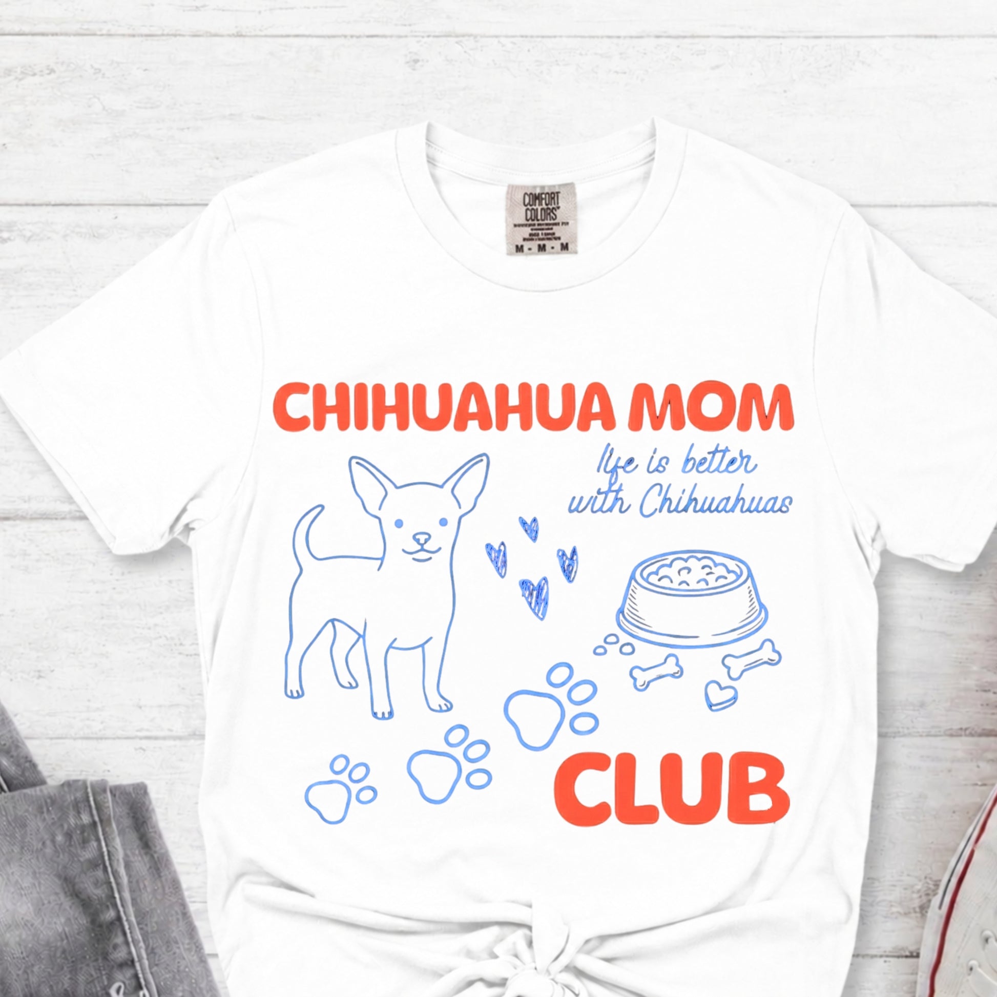 White t-shirt with 'Chihuahua Mom Club' text and graphics on a light wooden surface.