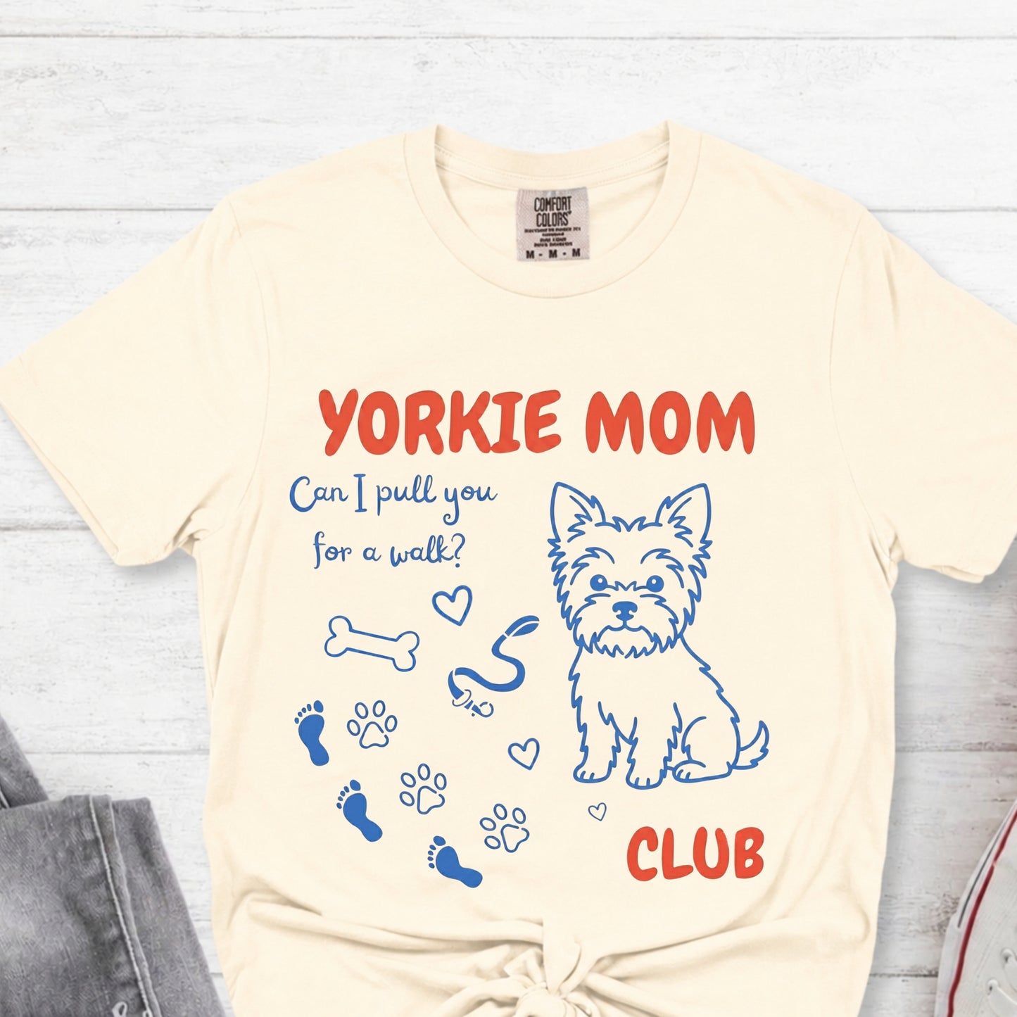 Beige t-shirt with Yorkie Mom graphic and text on a light wooden surface