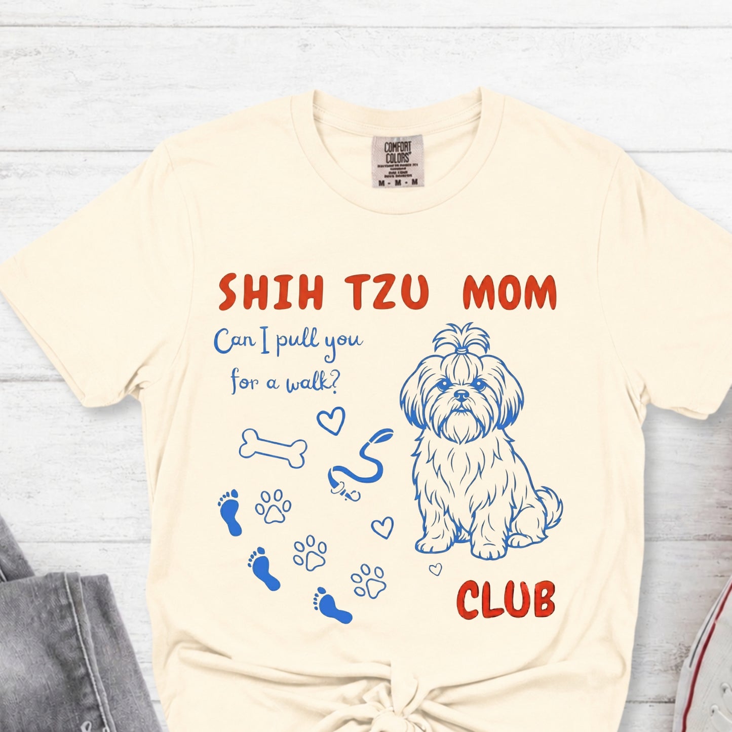 Beige t-shirt with Shih Tzu graphic and text on a light wooden surface