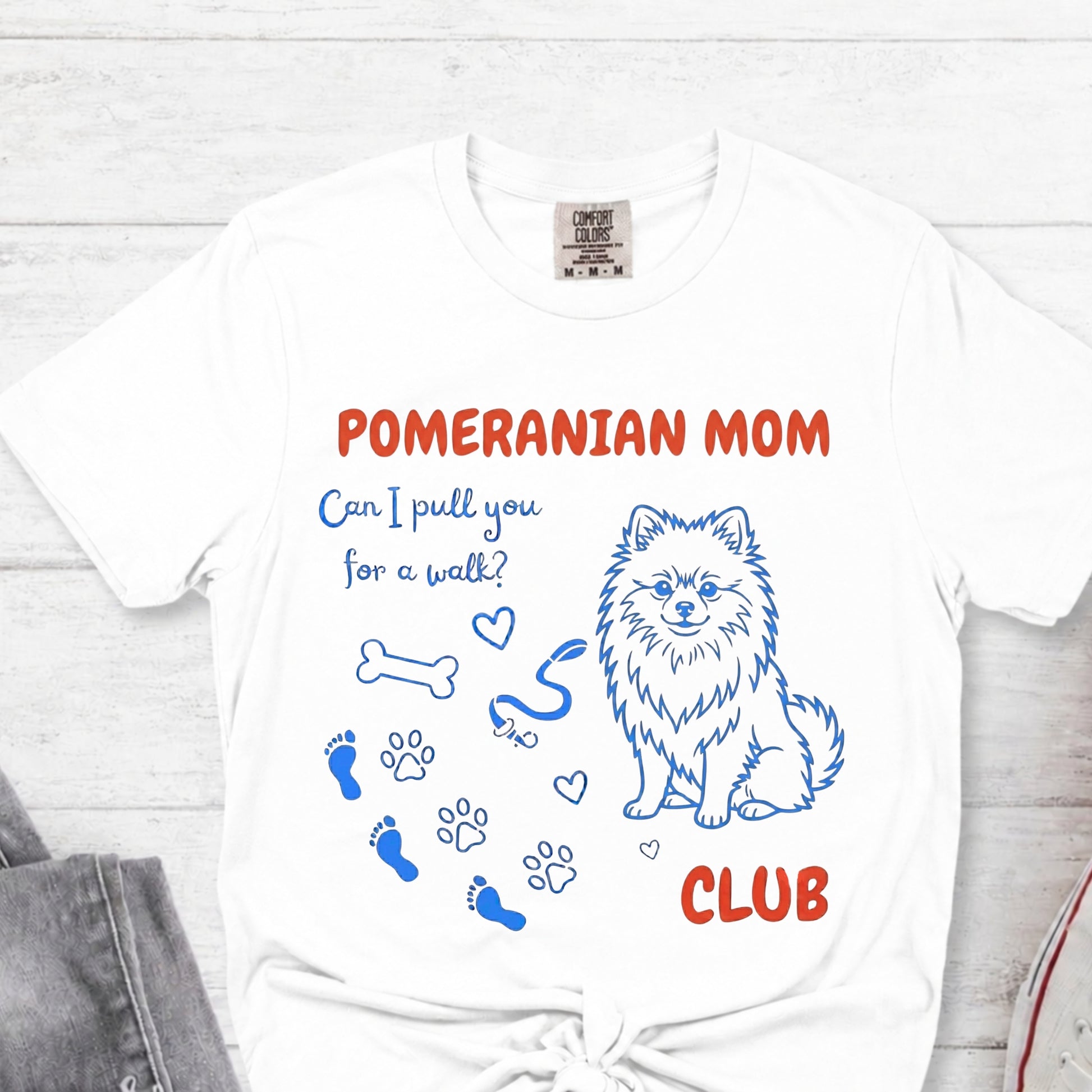 White t-shirt with Pomeranian-themed design and text on a light wooden surface.