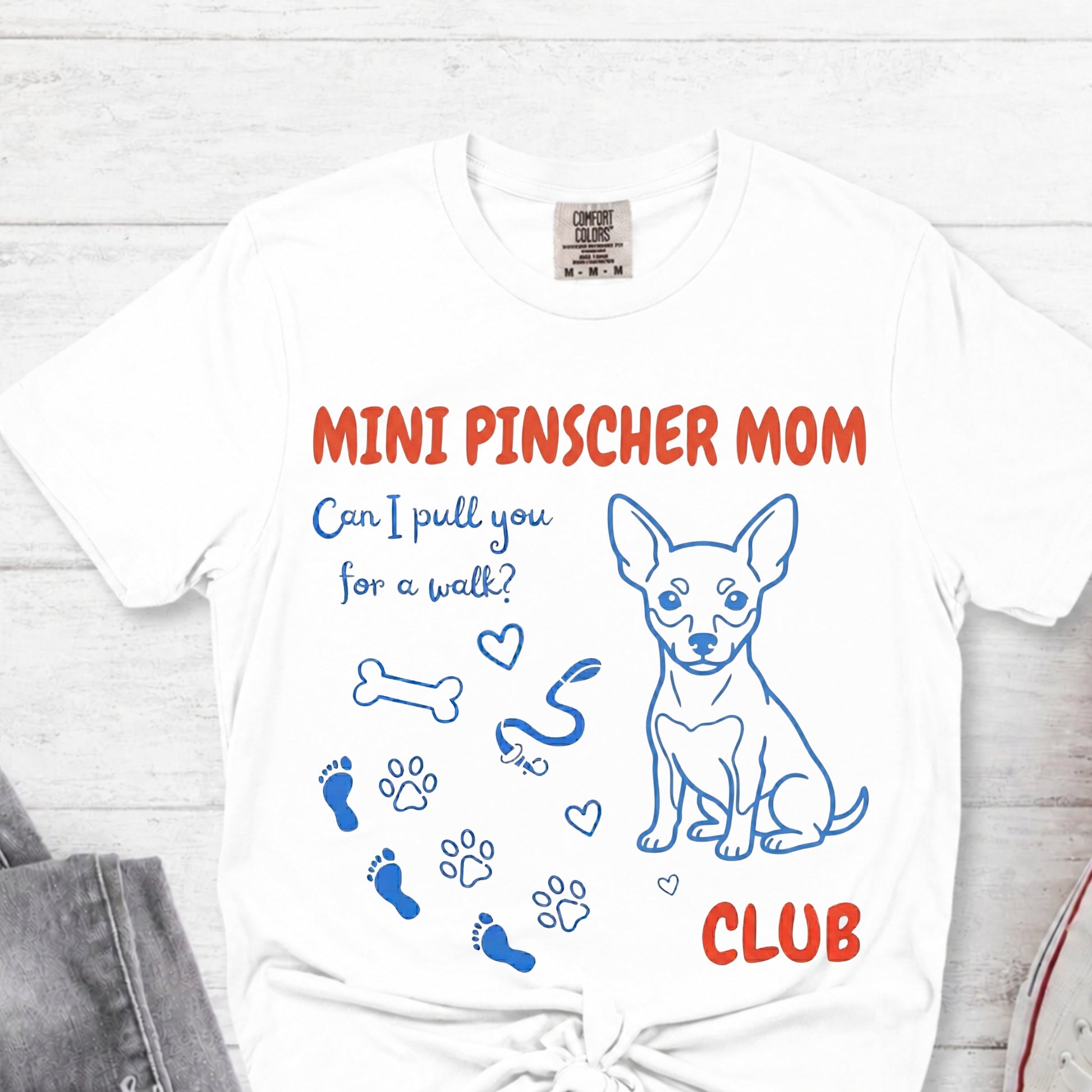 White t-shirt with 'Mini Pinscher Mom Club' design featuring a dog illustration and text on a white background.