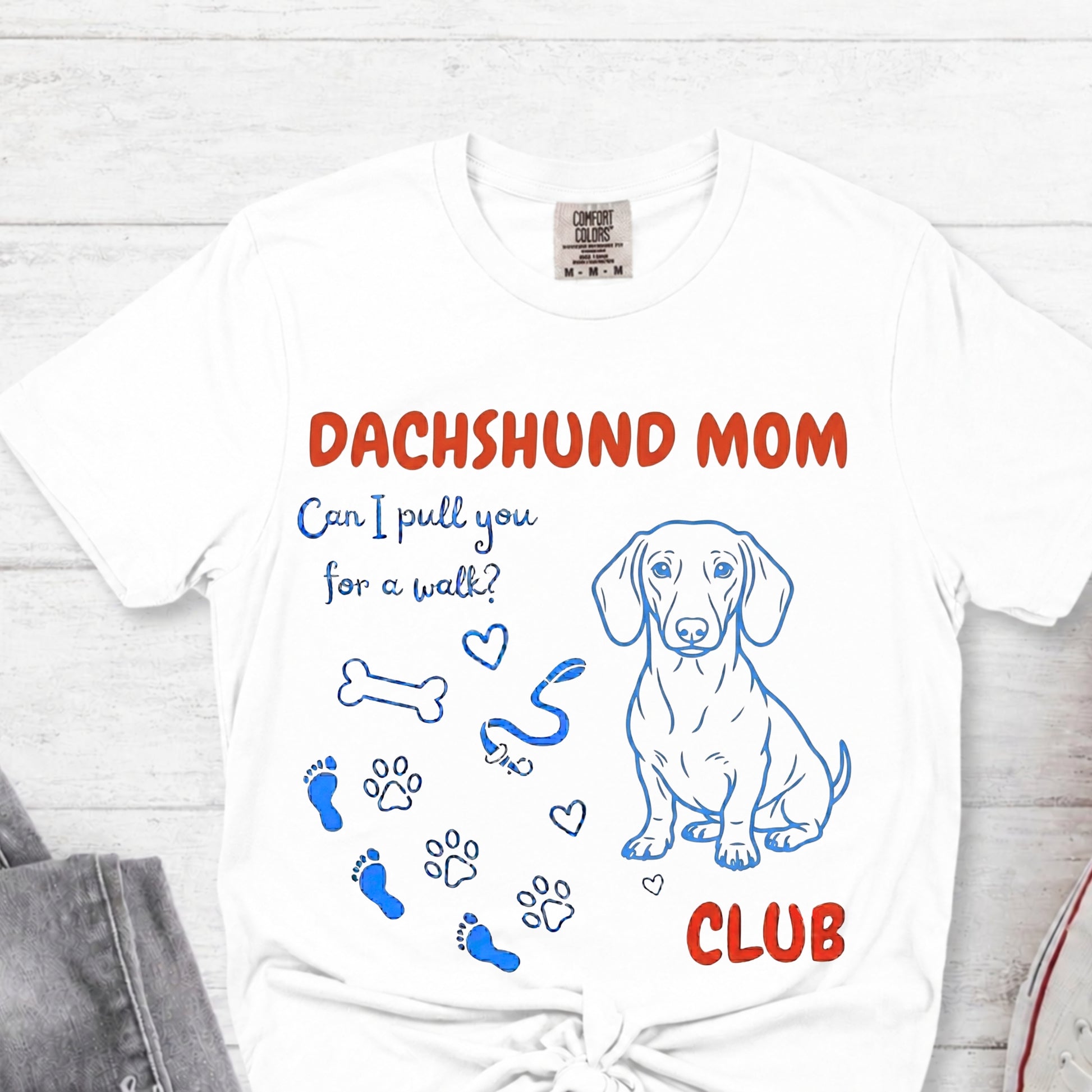 White t-shirt with 'FRENCHIE MOM' text and dog illustrations on a light wooden surface.