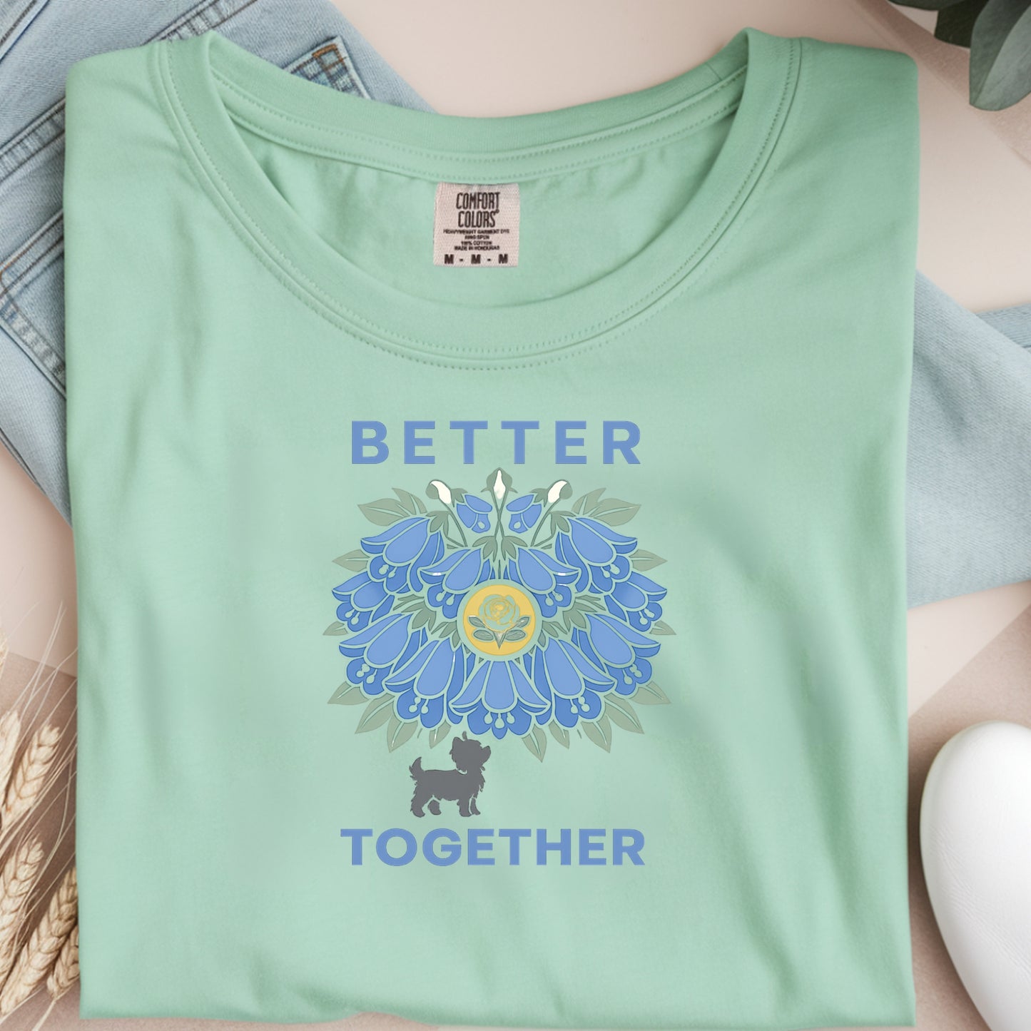 Light green t-shirt with blue floral design and 'Better Together' text on a neutral background