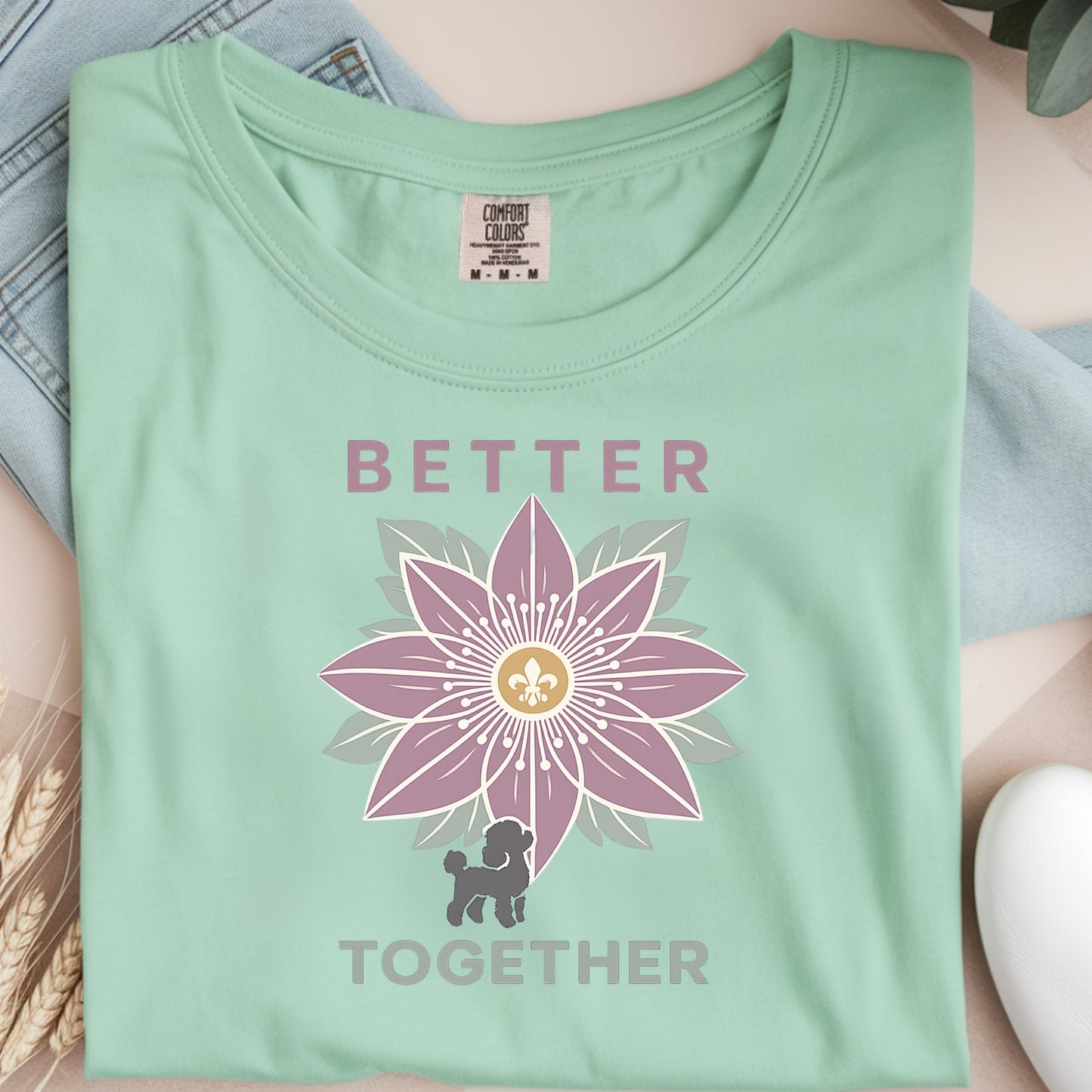 Folded light green t-shirt with a purple flower design and text on a neutral background