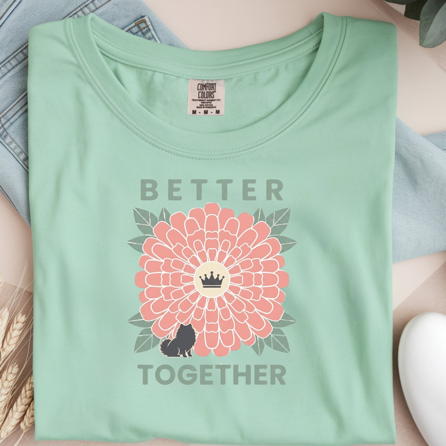 Light green t-shirt with a pink flower and text design on a neutral background