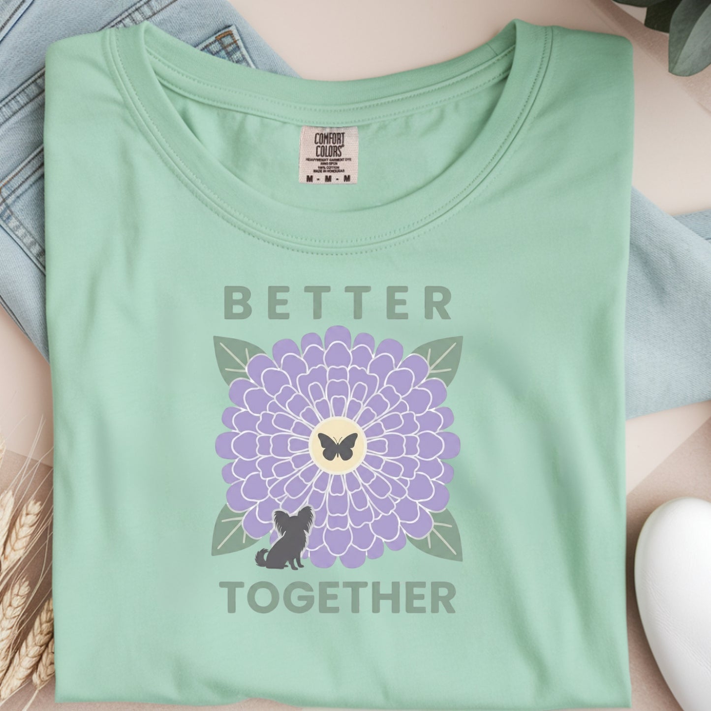 Light green t-shirt with a purple flower and text design on a neutral background