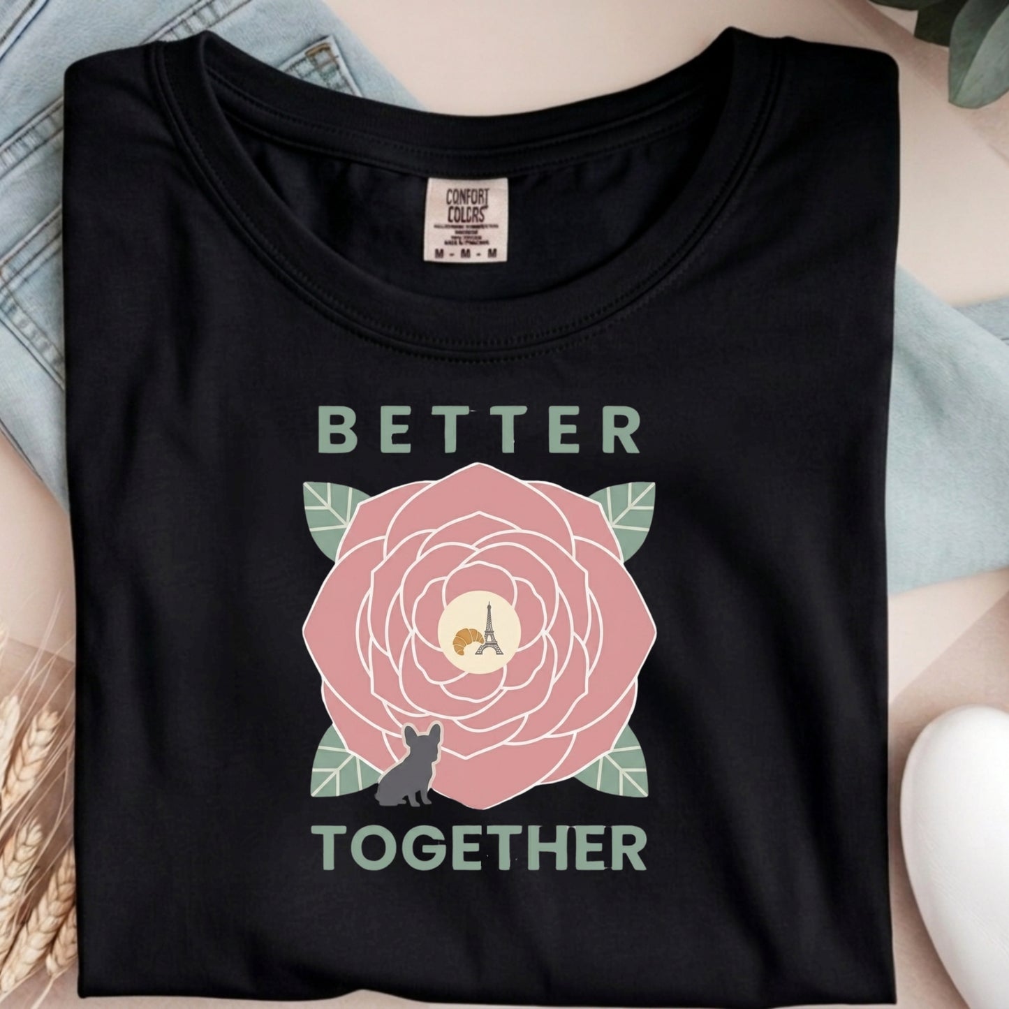 Black t-shirt with a pink flower graphic and 'Better Together' text on a light blue fabric background.
