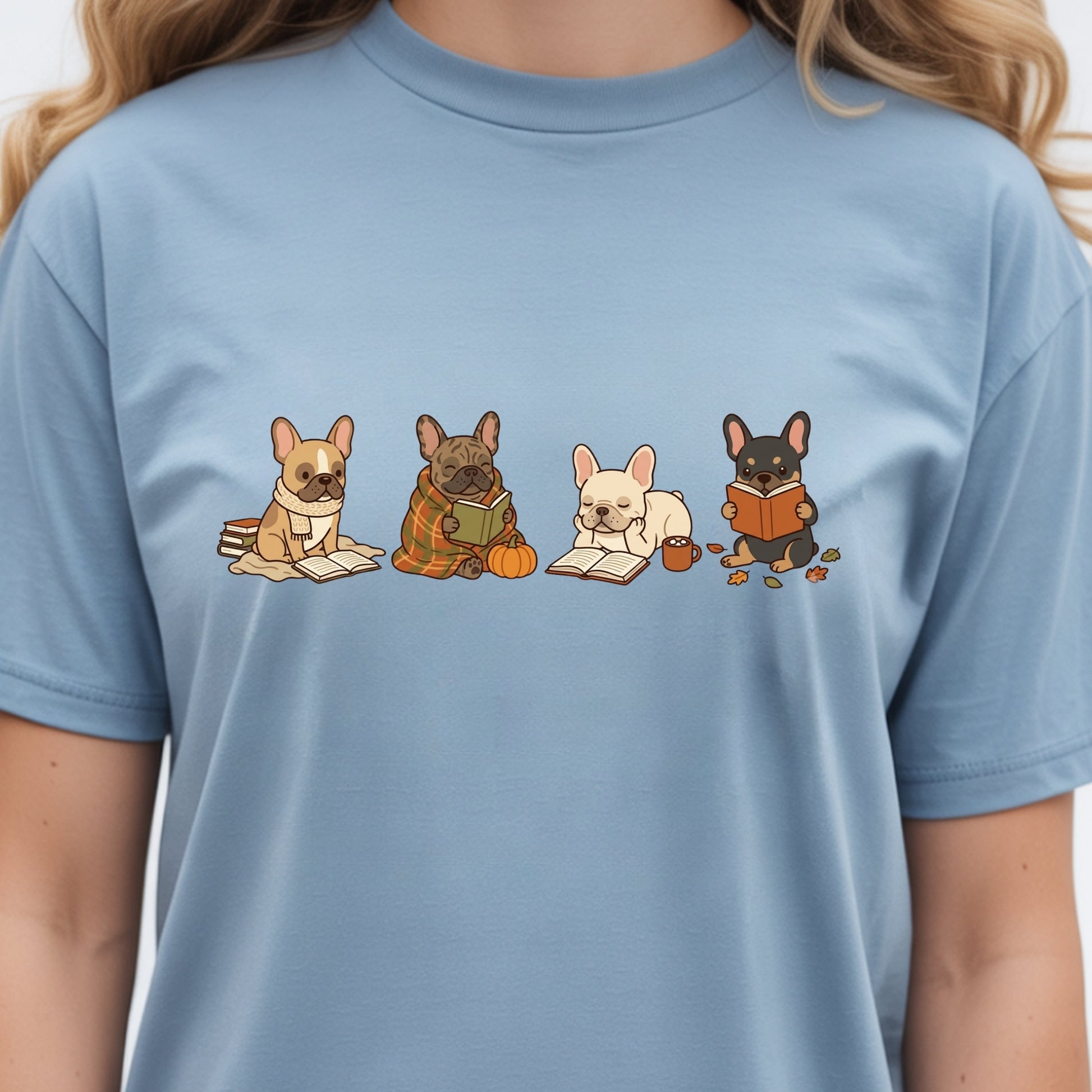 A person wearing a light blue crewneck t-shirt with a graphic print of four cute French bulldogs reading books.