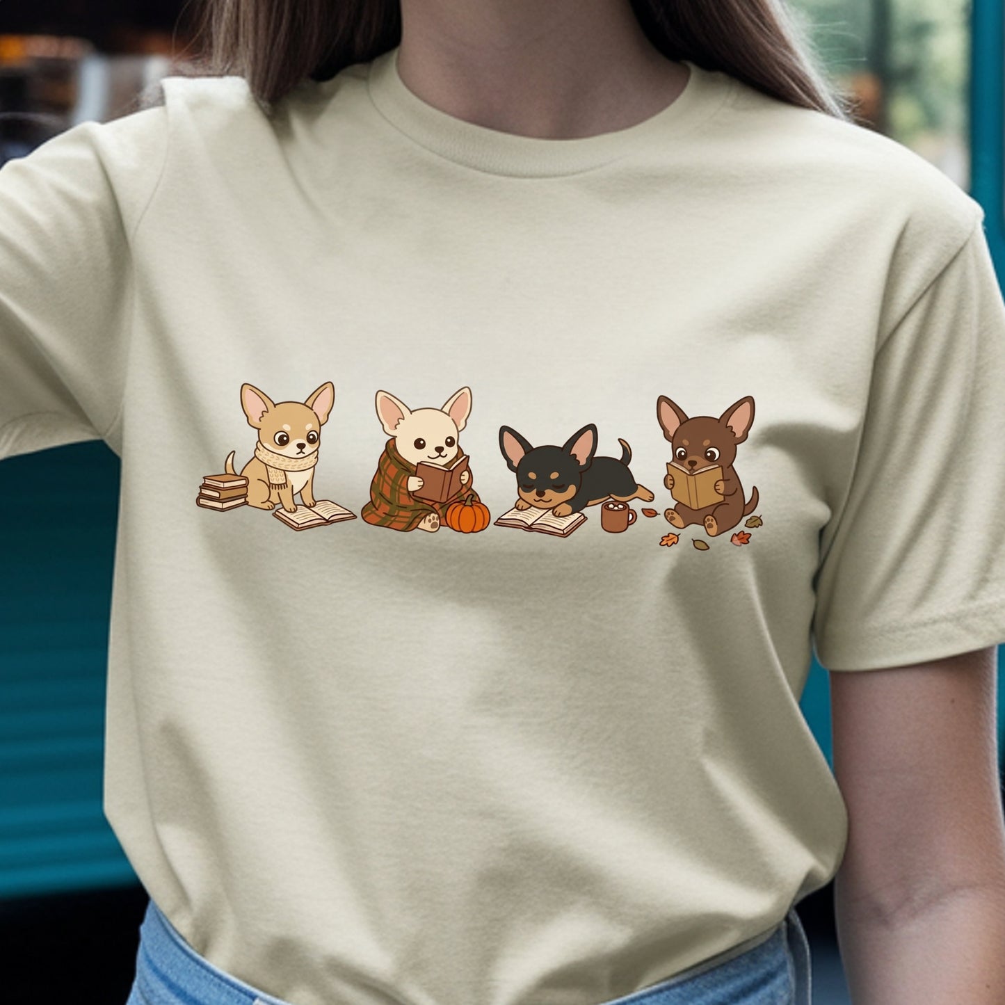 A person wearing a light beige crewneck t-shirt with a graphic print of four cute cartoon Chihuahua dogs reading books.