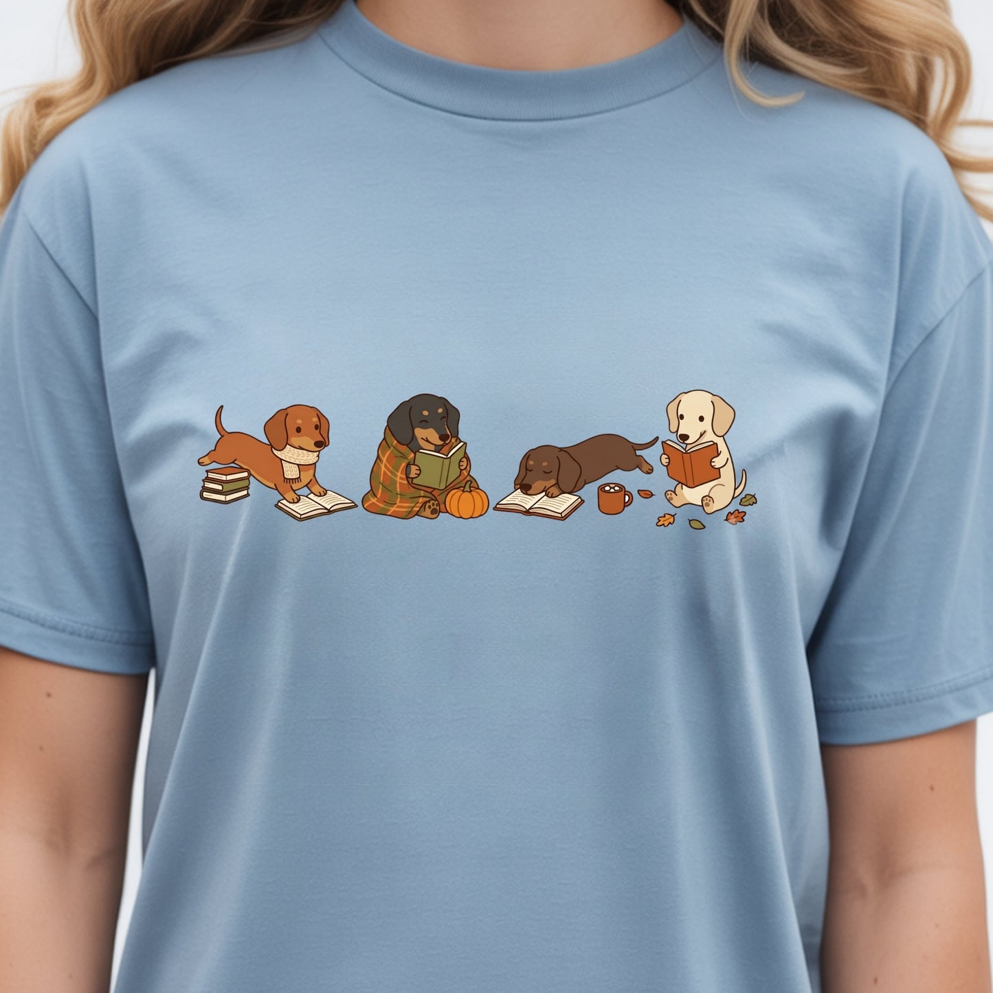 A light blue crewneck t-shirt featuring a graphic print of four cute cartoon dogs reading books, worn by a model.